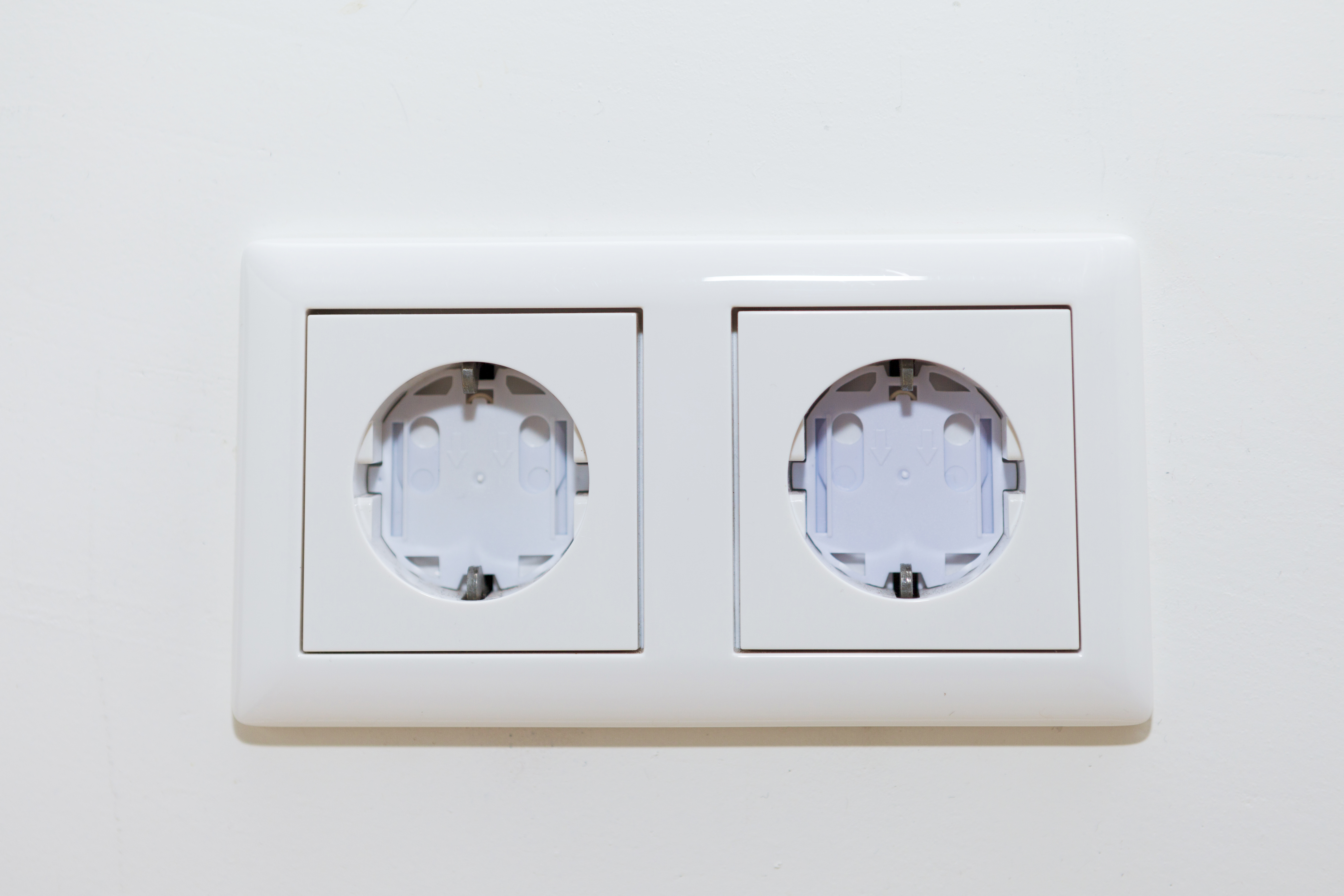 Zwei weiße Steckdosen nebeneinander an einer weißen Wand. Keine Stecker eingesetzt.