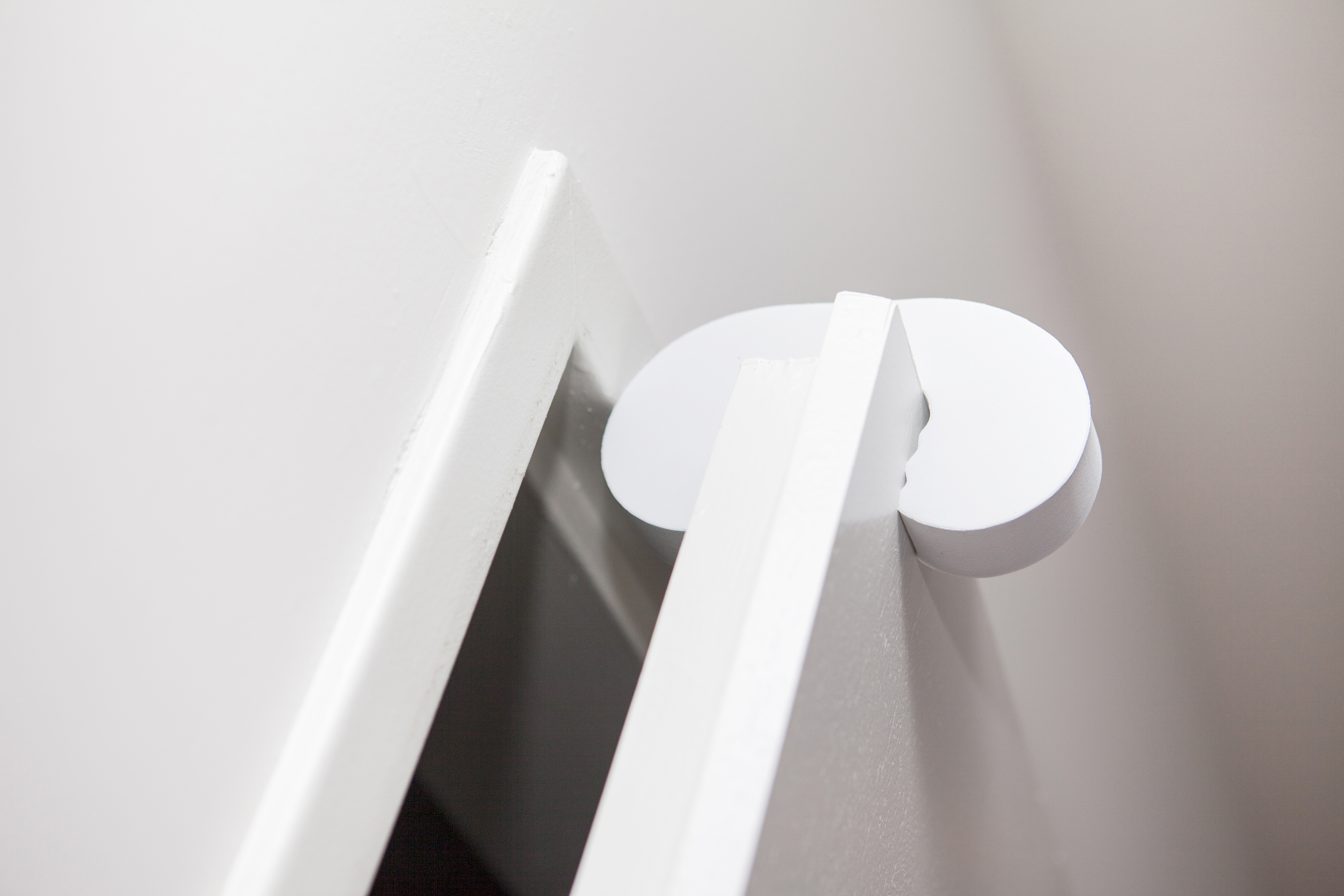 Eine weiße Tür mit einem weißen Türstopper in geöffneter Position, weiße Wand.