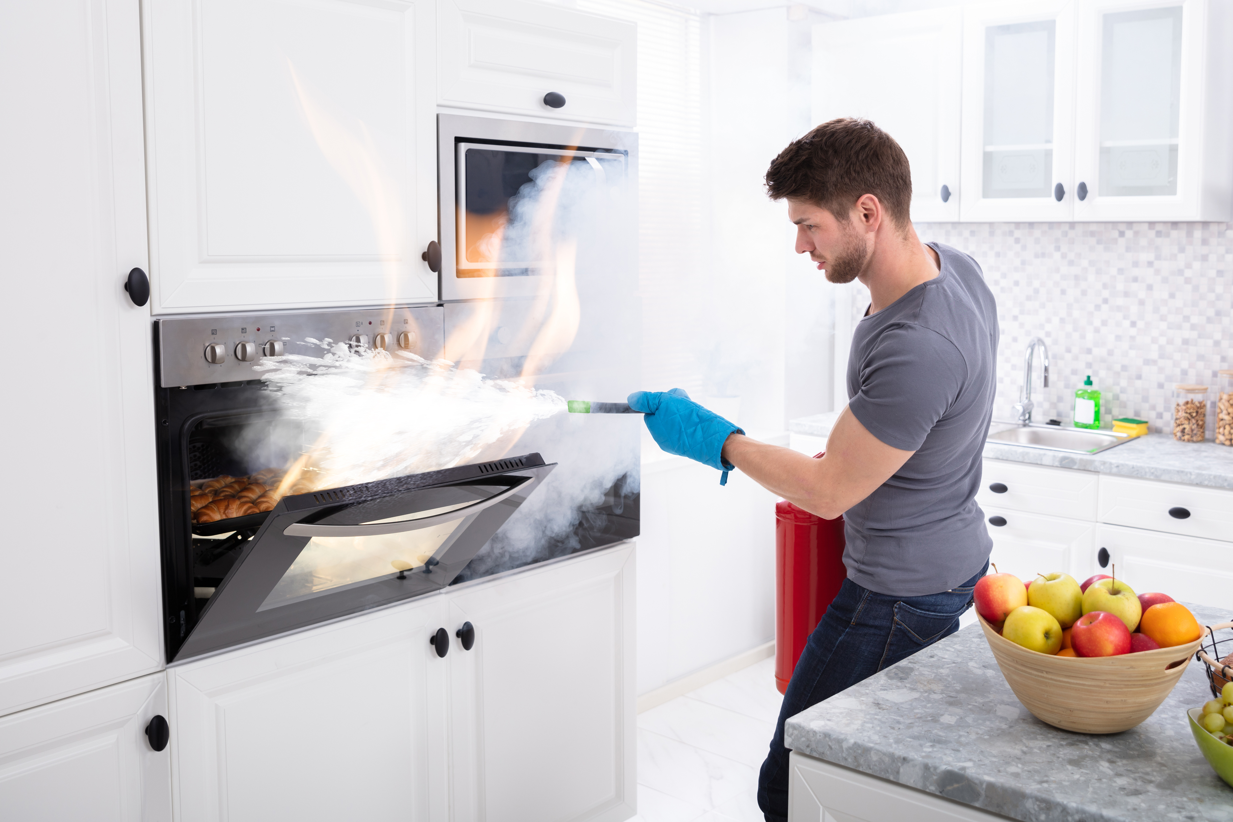 Un homme dans une cuisine utilise un extincteur pour éteindre un feu dans un four.