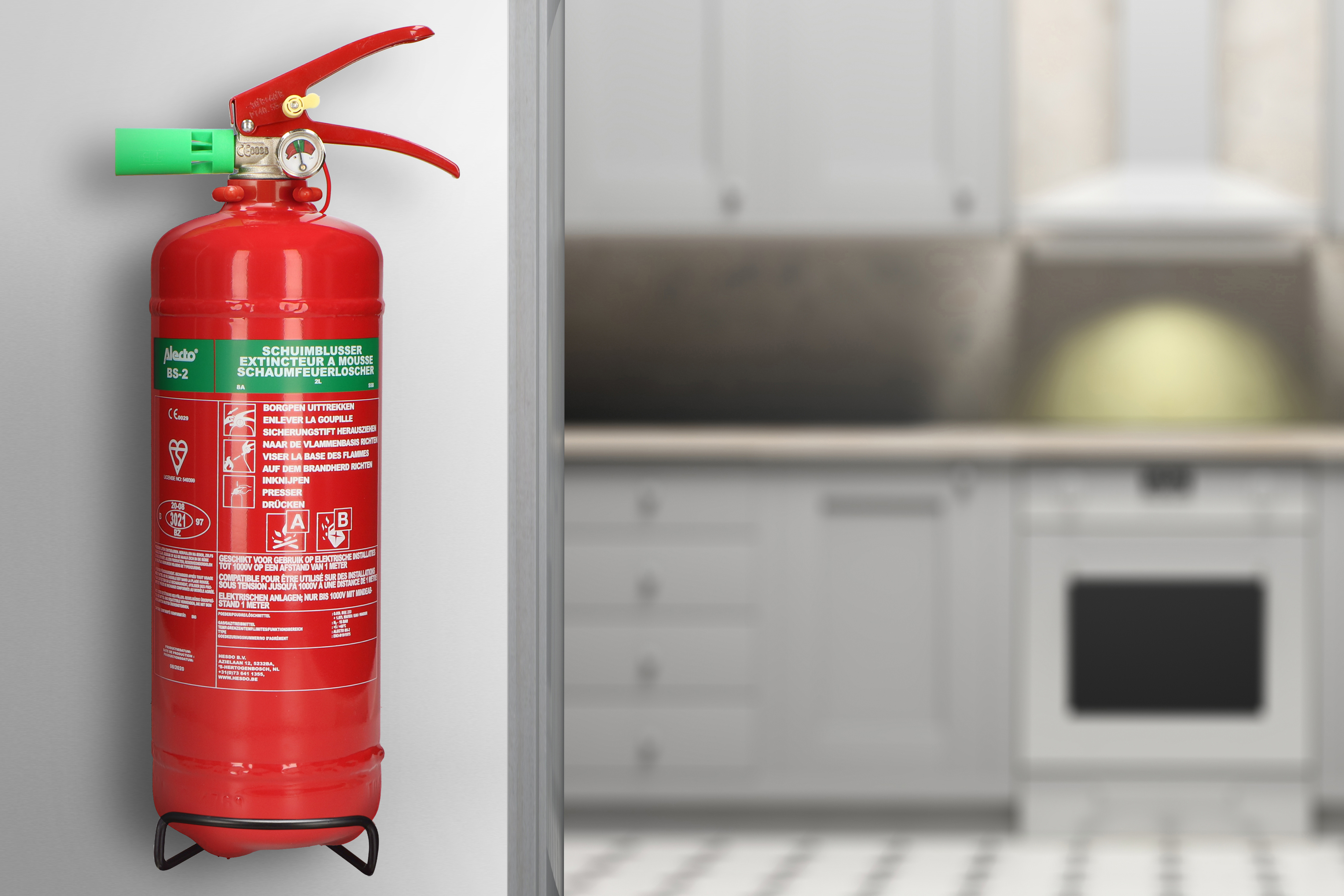 Red fire extinguisher mounted on a wall in a kitchen setting. Green nozzle and handle.