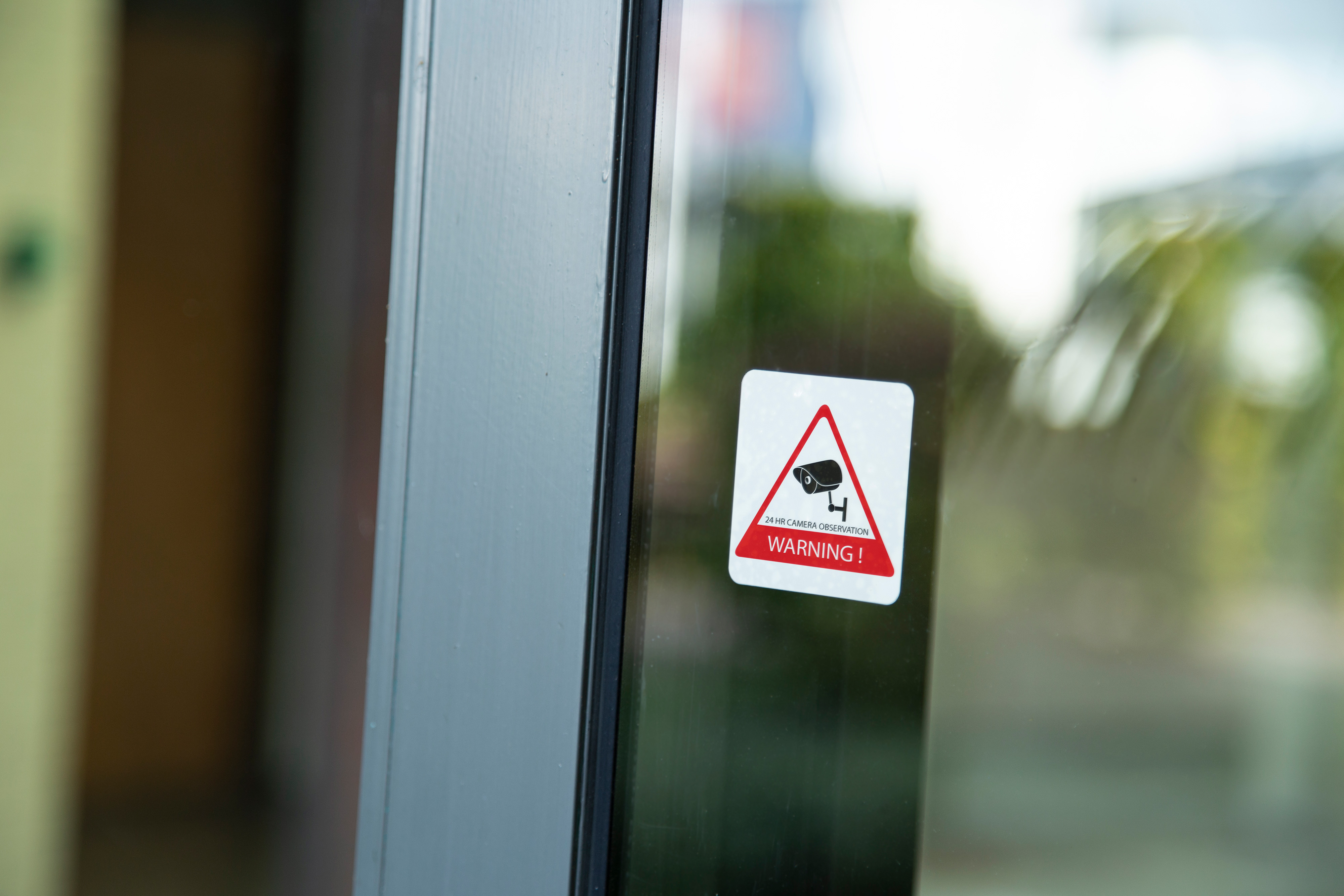 A warning sign on a glass door. It features a camera icon and a red triangle.