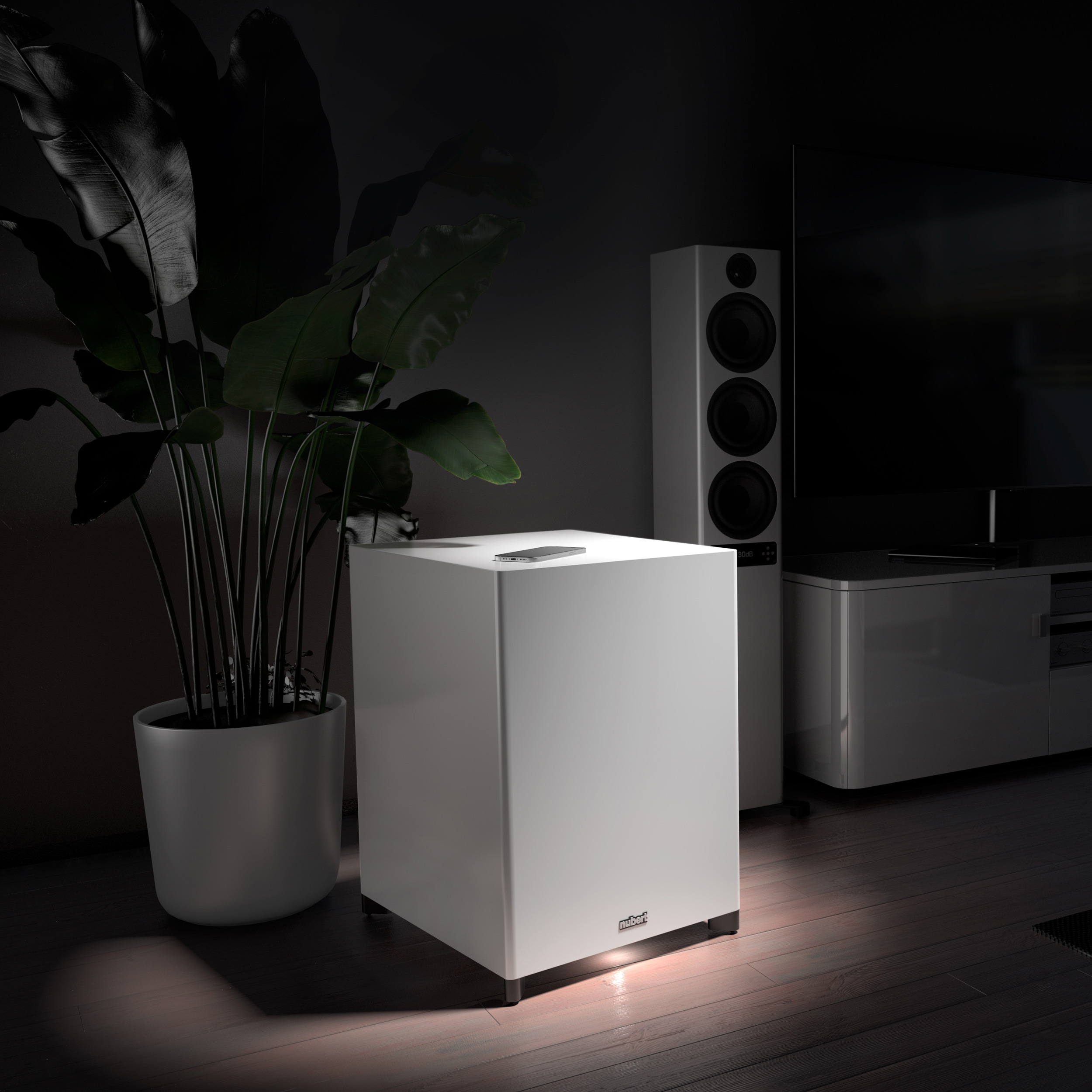 Ein weißer Subwoofer steht in einem dunklen Raum neben einer Pflanze und Lautsprechern.