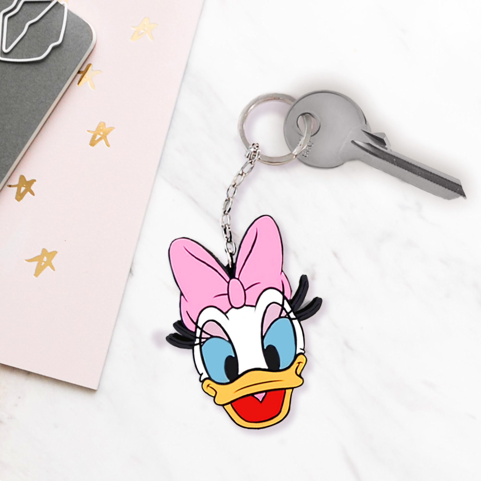 Brelok Daisy Duck z różową kokardą, kluczami i notatnikiem z gwiazdami.