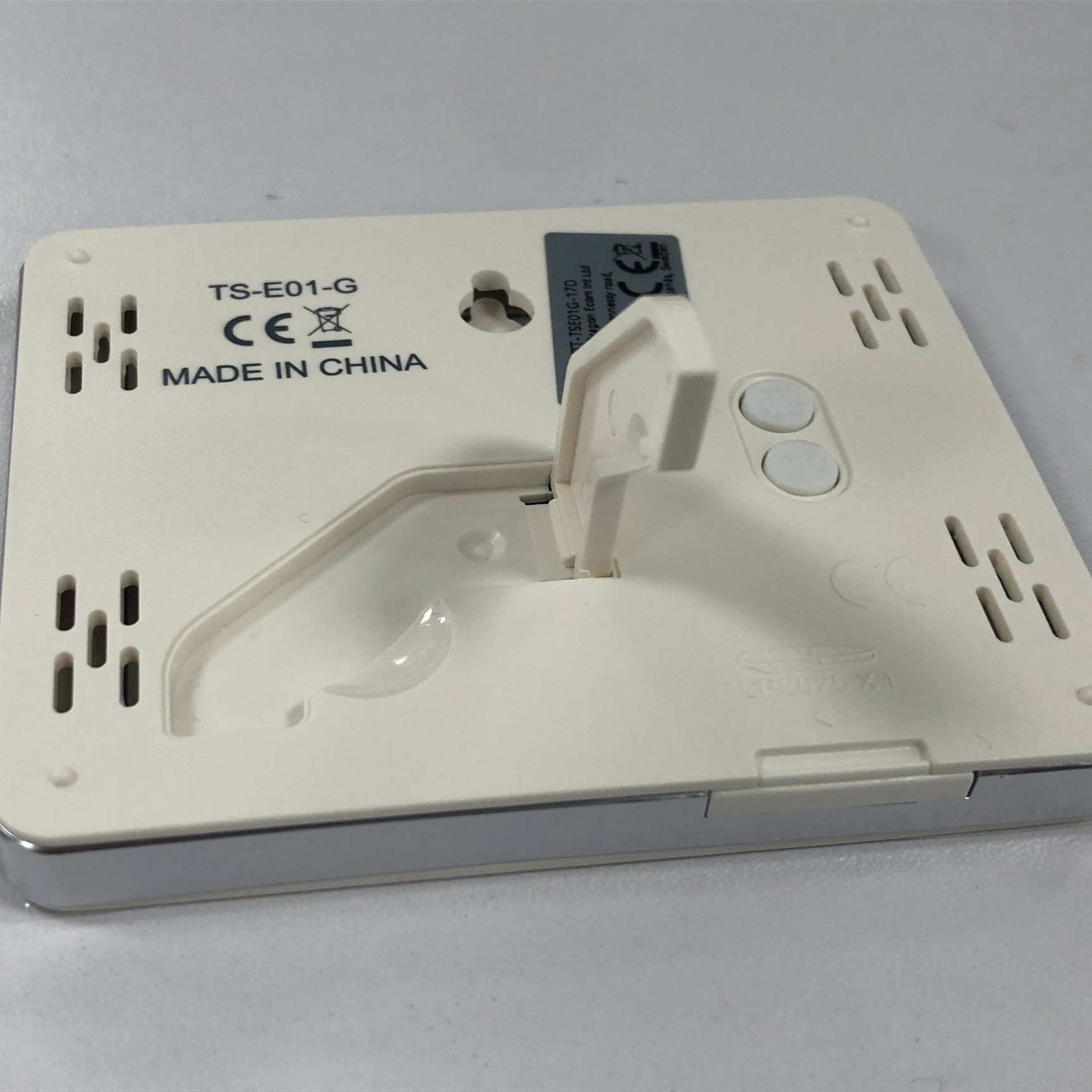 Unterseite eines weißen quadratischen Geräts. Es hat einen Klappständer und zwei Knöpfe. Made in China steht drauf.