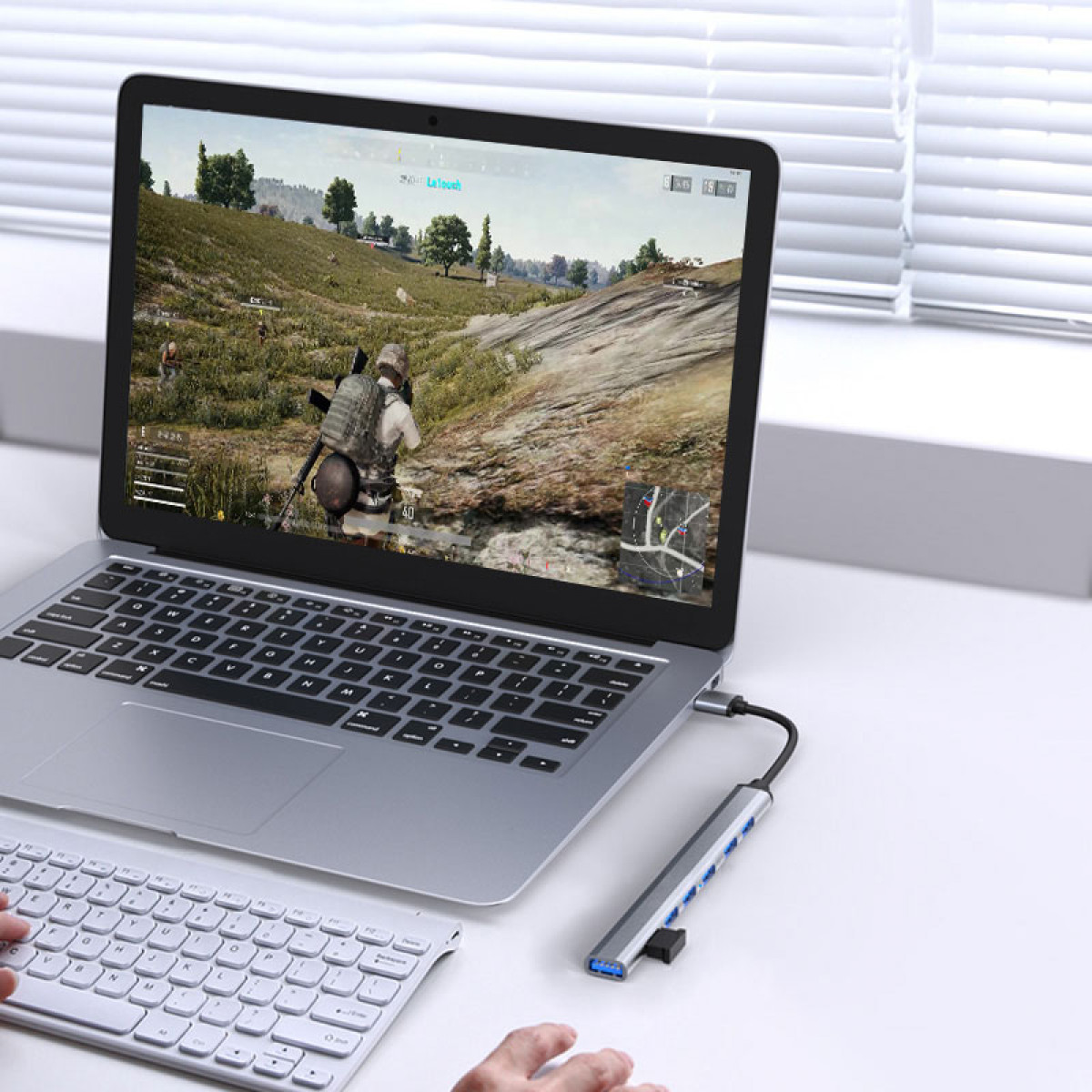 Laptop z grą na ekranie, podłączony do huba. Ręka używa klawiatury.