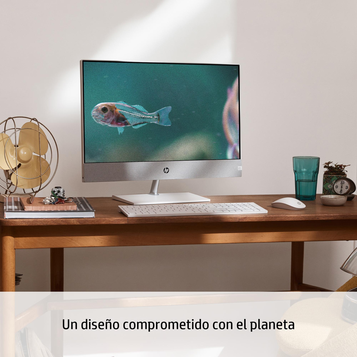 Configuración de computadora con monitor mostrando peces, ventilador, vaso y reloj en el escritorio.