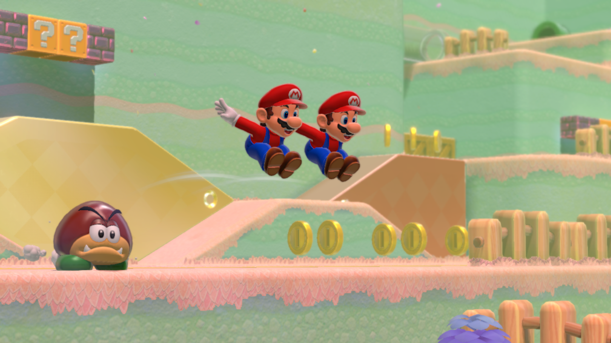 Due personaggi di Mario che saltano in un livello colorato con monete, Goomba e blocchi punto interrogativo.