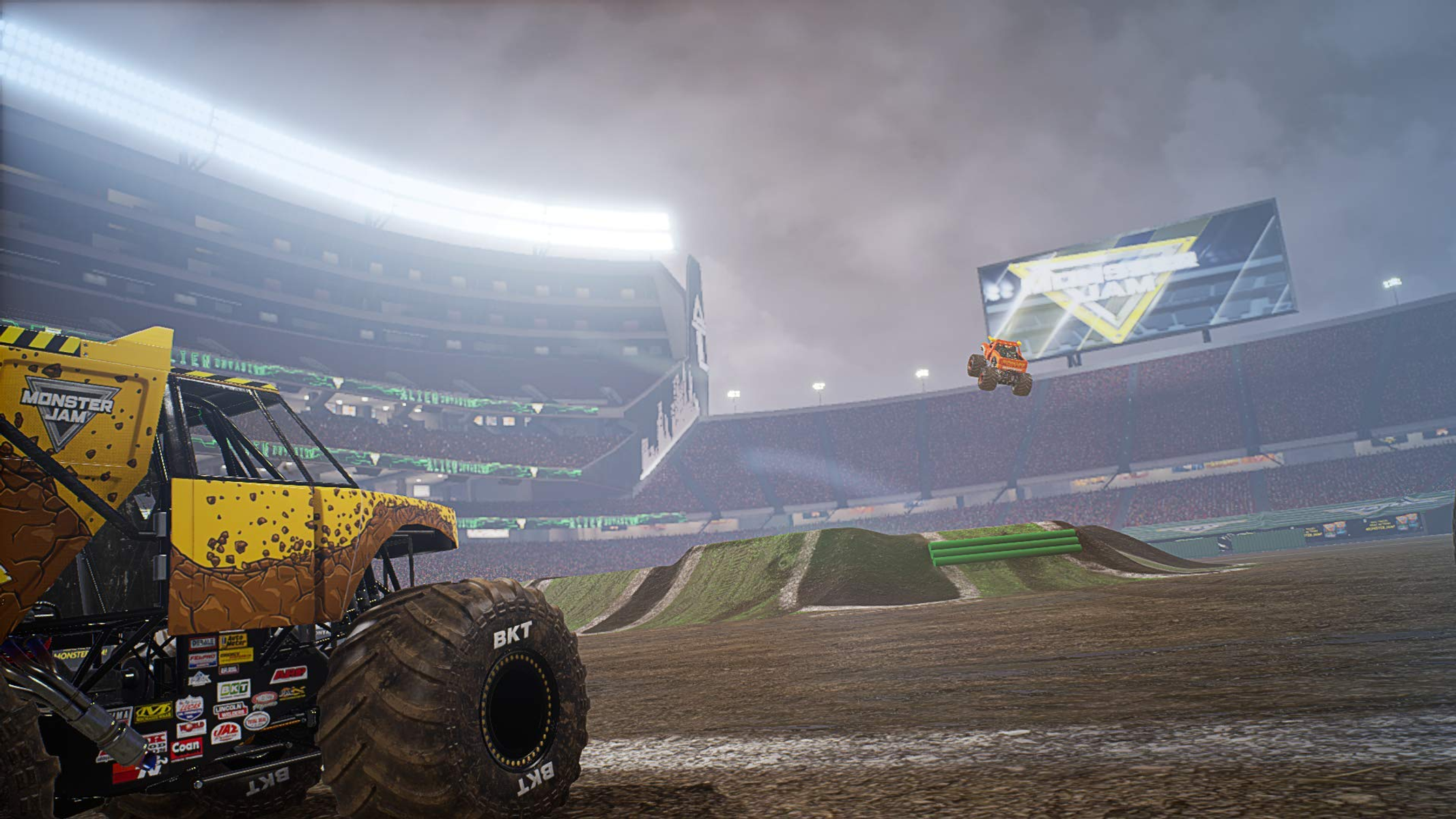 Camion Monster Jam nell'arena. Camion giallo a sinistra. Un altro camion salta sullo sfondo.