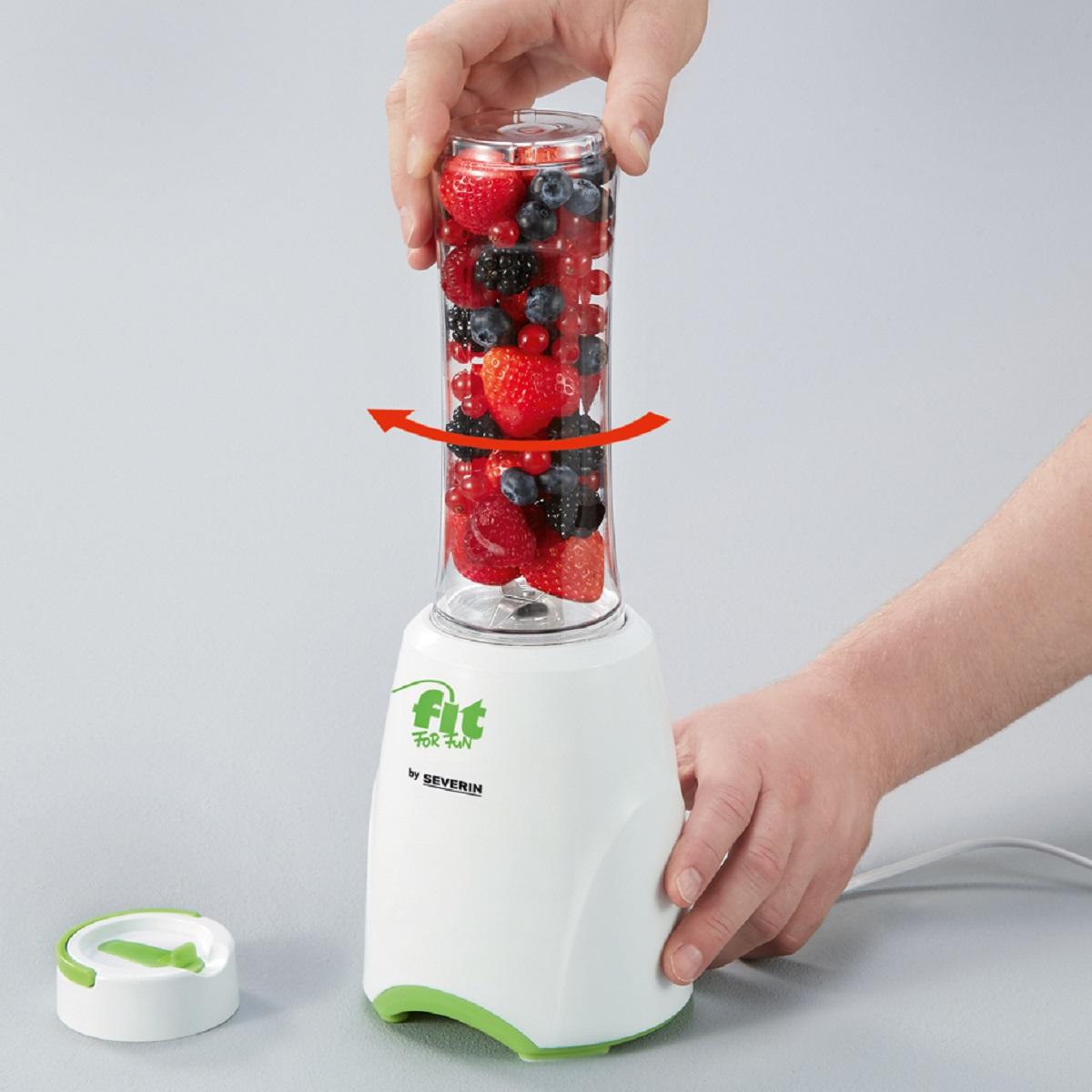 Blender gevuld met gemengde bessen, met handen die de bovenkant vasthouden.