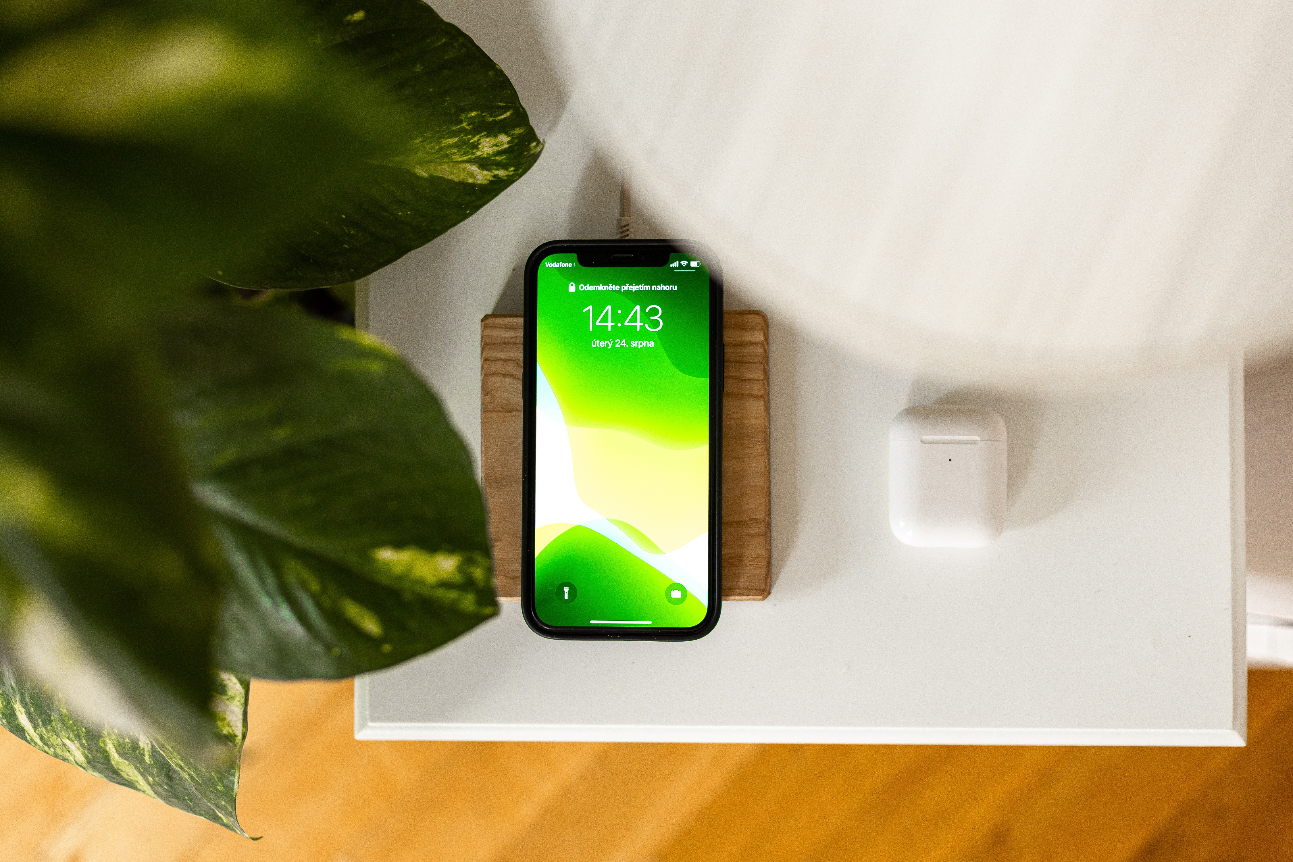 Ein Telefon auf einem Holzständer, das Zeit und Datum anzeigt. Weiße Ohrhörer sind in der Nähe.