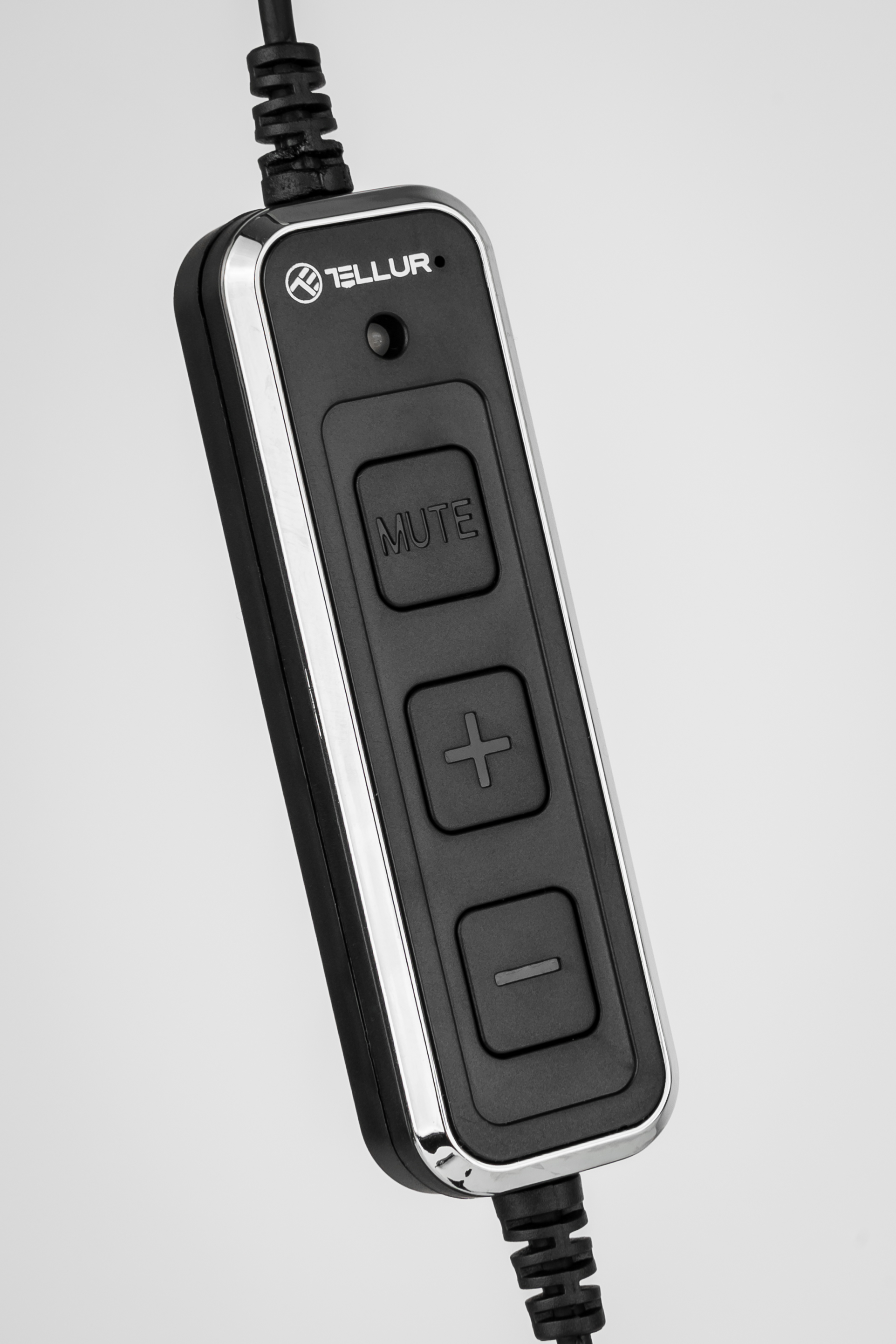 Czarna kontrola audio na przewodzie. Posiada przyciski wyciszania, zwiększania i zmniejszania głośności. Tło jest białe.