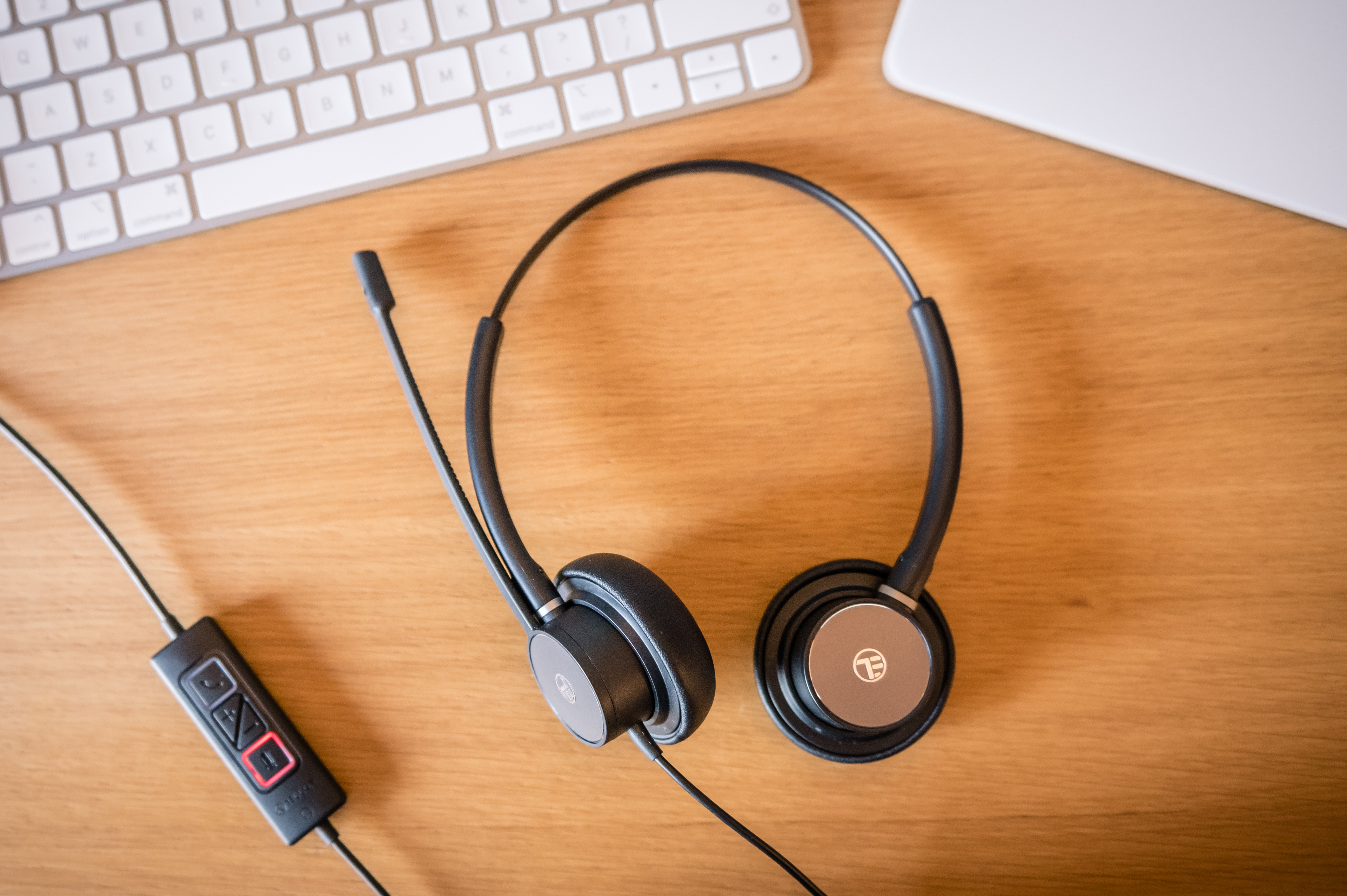 Czarny i srebrny zestaw słuchawkowy z mikrofonem, na drewnianym biurku z klawiaturą i laptopem.