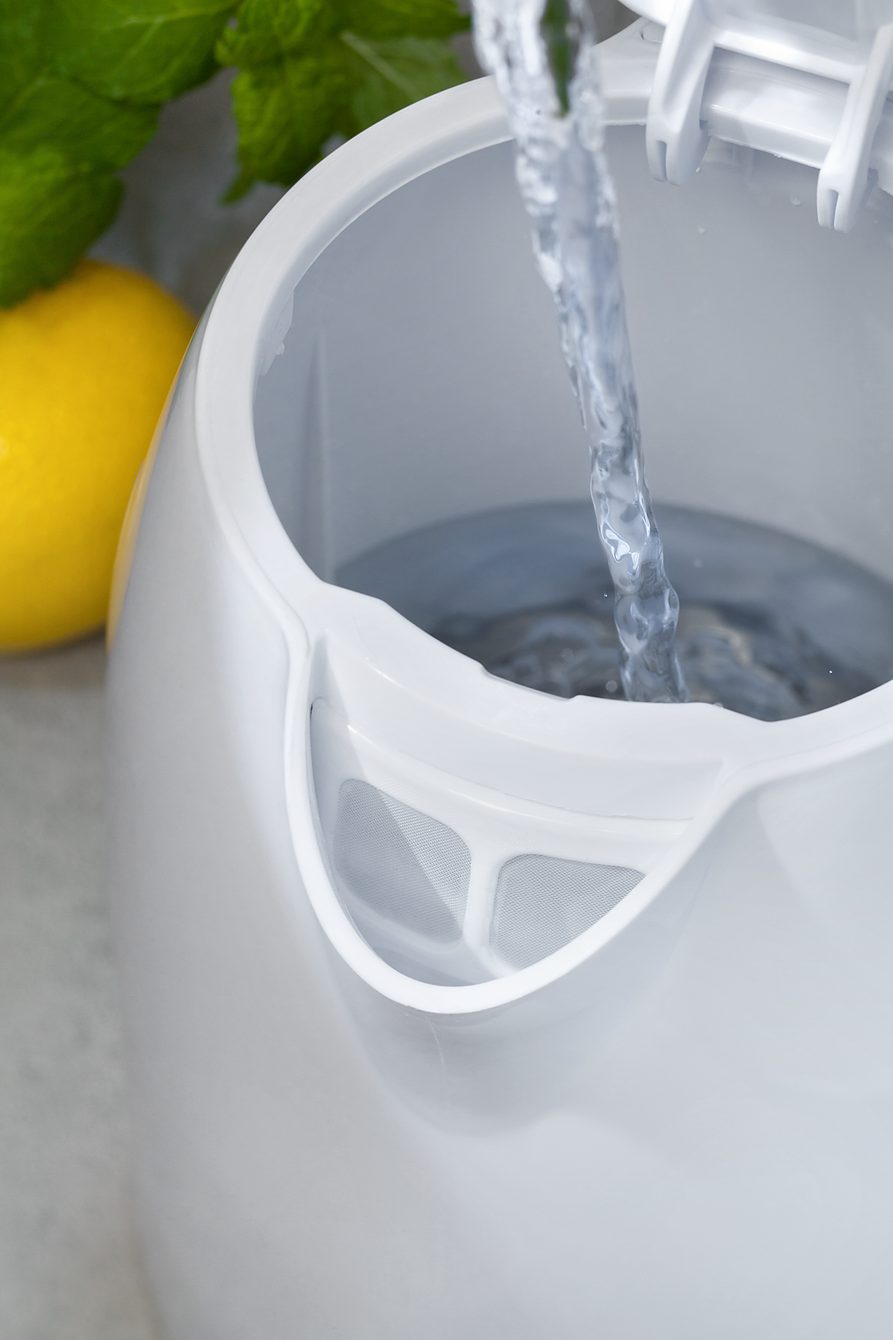 Agua se vierte en una tetera blanca. Un limón y hojas de menta están en el fondo.