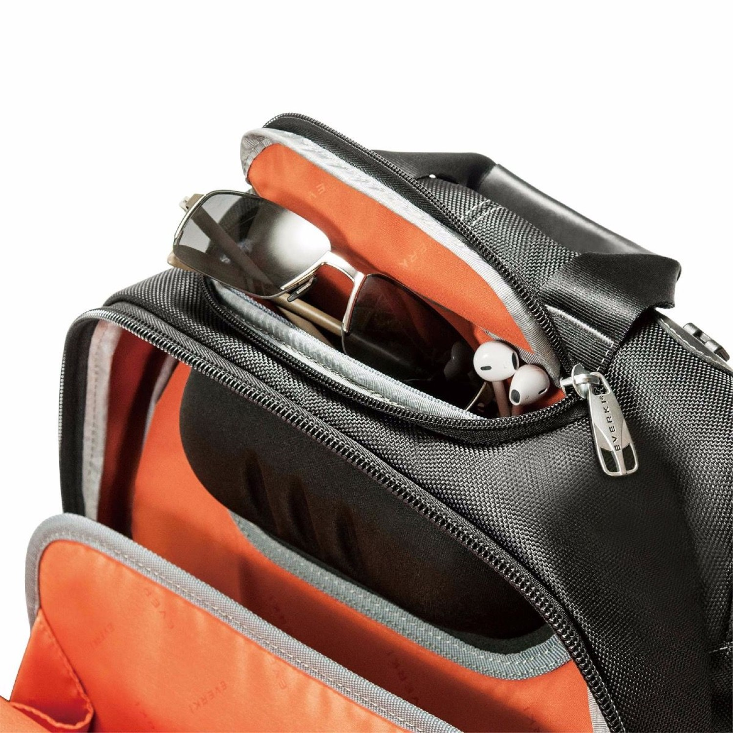 Schwarze Tasche offen, Sonnenbrille und Kopfhörer sichtbar. Innen orange.