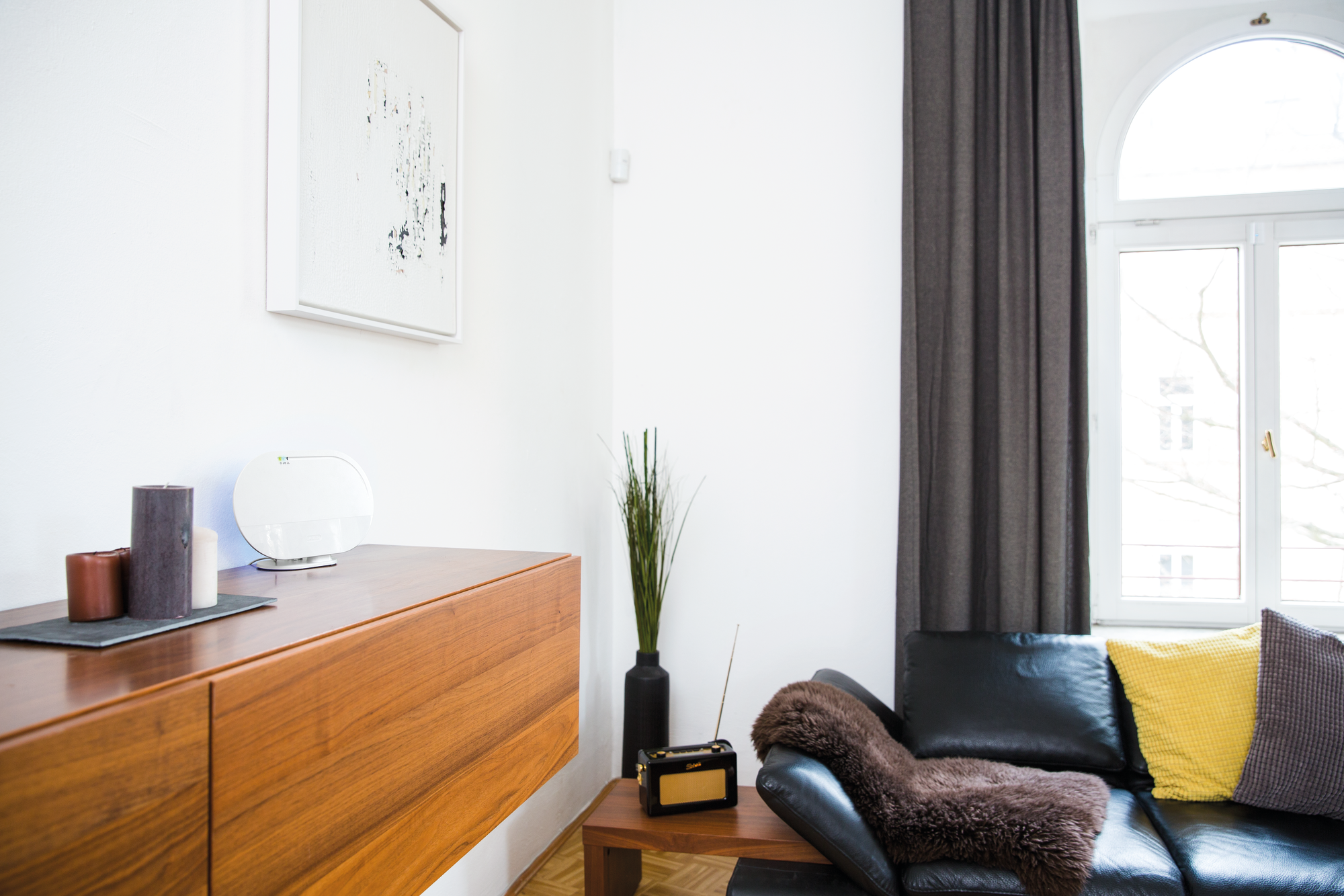 Wohnzimmer mit Holzschrank, schwarzem Sofa und Kunst an der Wand.