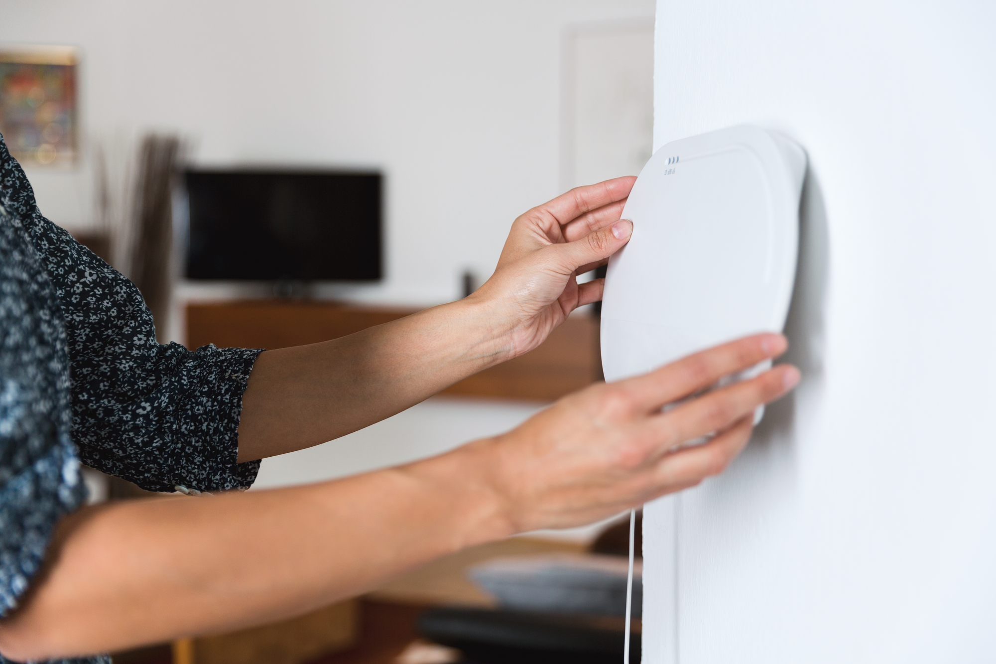 Eine Person installiert ein weißes Gerät an einer Wand. Das Gerät ist oval geformt.