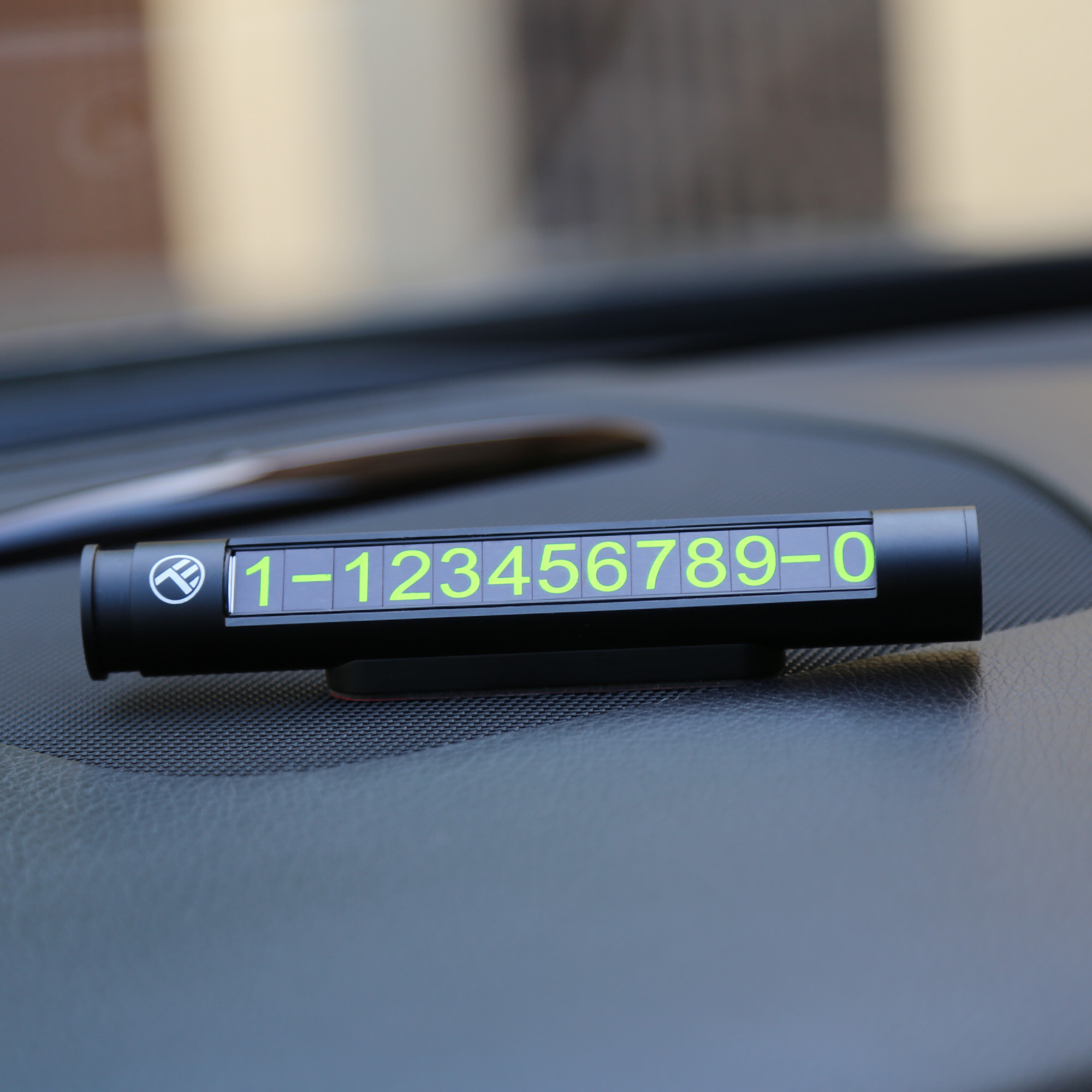 Wyświetlacz numeru telefonu samochodowego z zielonymi cyframi. Leży na desce rozdzielczej samochodu.