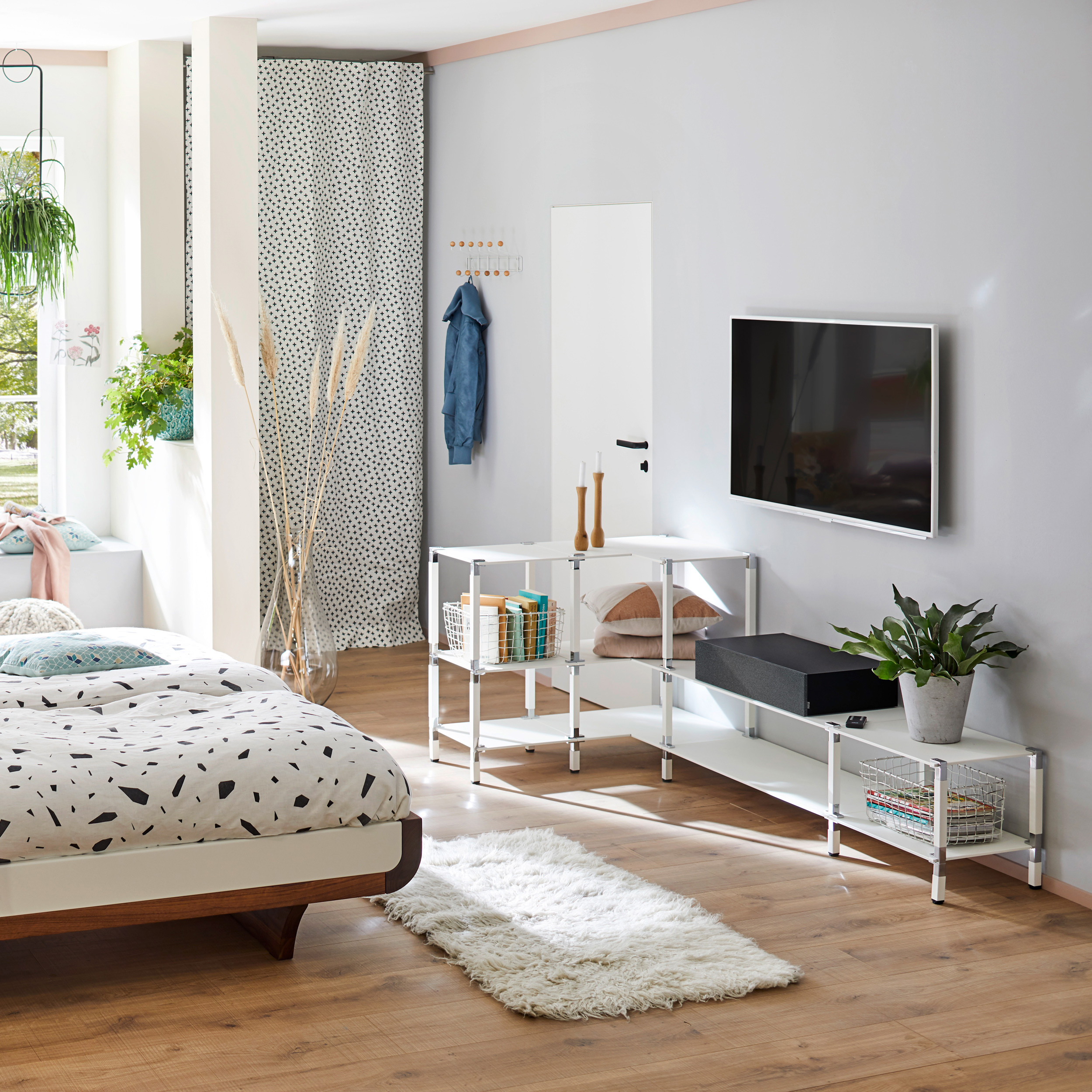 Schlafzimmer mit Bett, Fernseher an der Wand, Regalen und einem weißen Teppich.