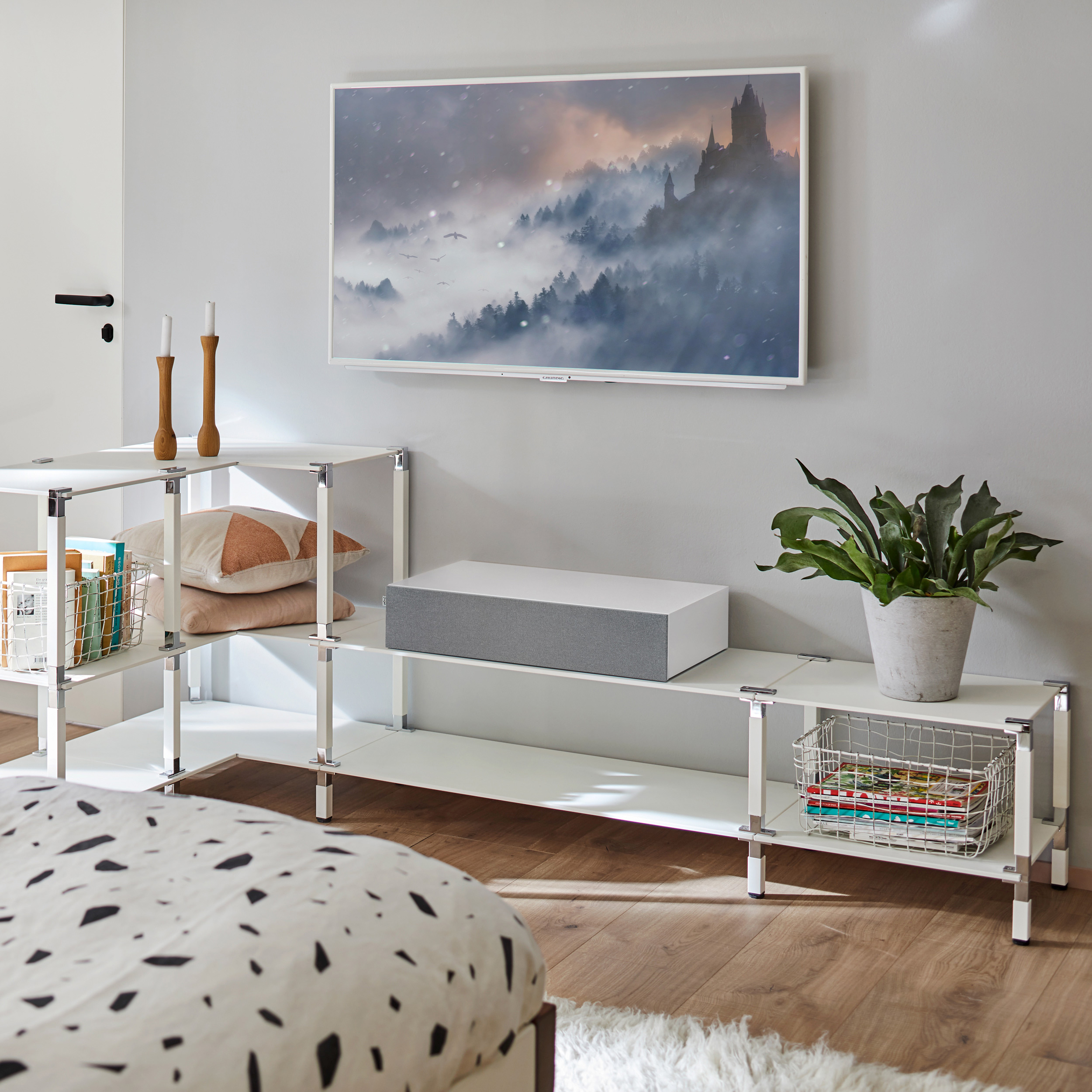 Schlafzimmer mit weißem Mobiliar, TV mit Landschaft, Bett mit schwarz-weiß gemusterter Bettdecke.