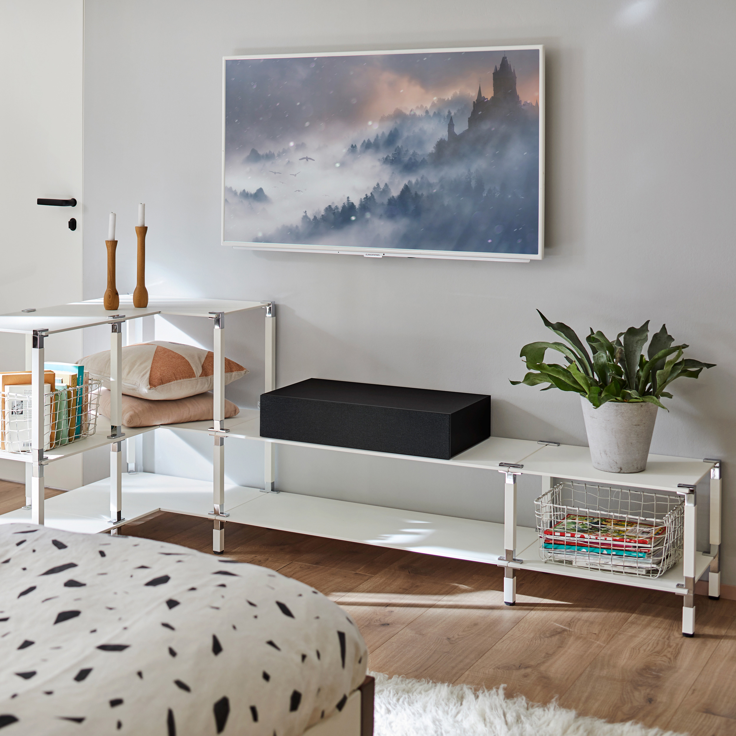Ein modernes Wohnzimmer mit weißen Regalen, einem Fernseher und dekorativen Elementen. Der Raum ist hell.