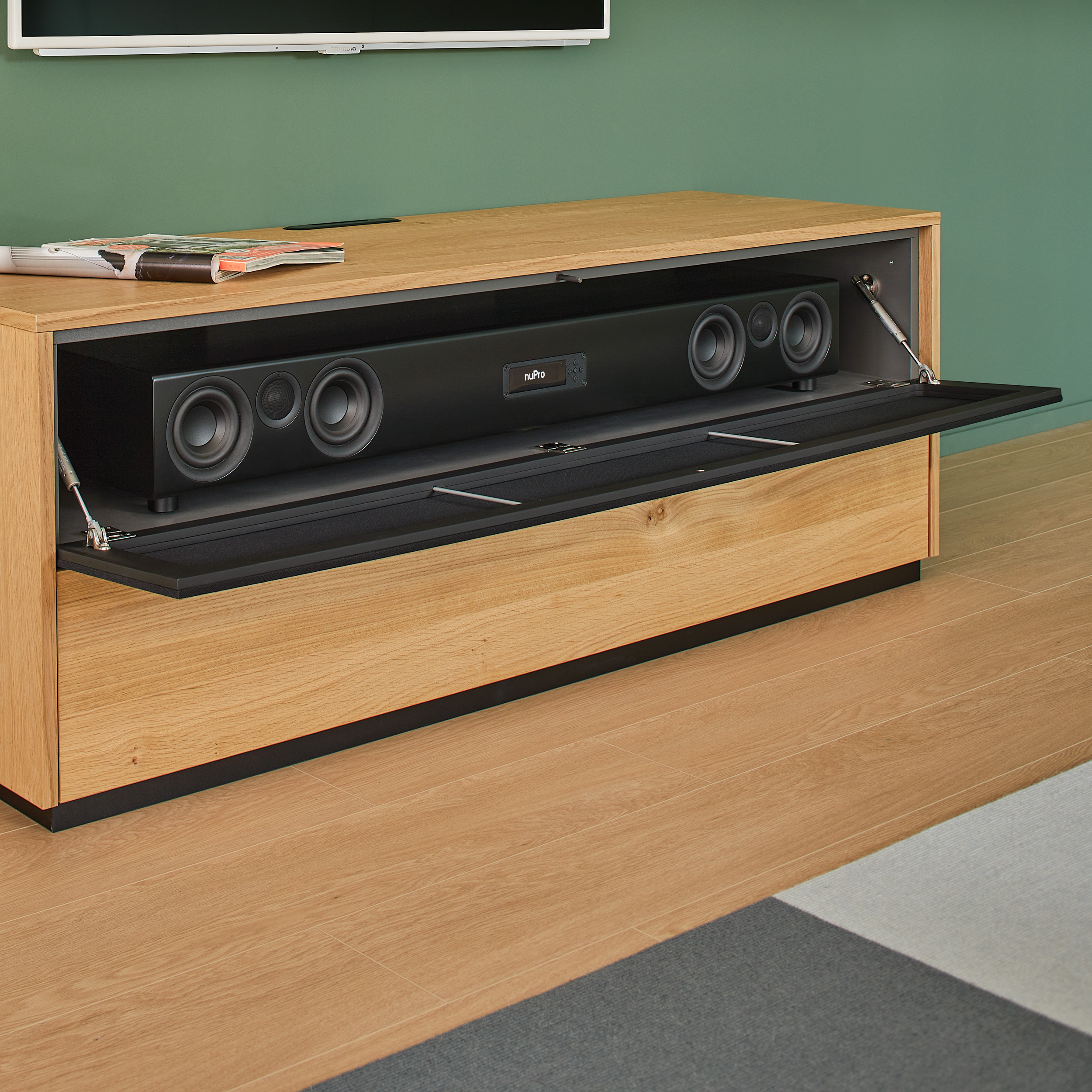 TV-Schrank aus Holz mit offenen Türen, die eine schwarze Soundbar und Lautsprecher zeigen, grüne Wand.