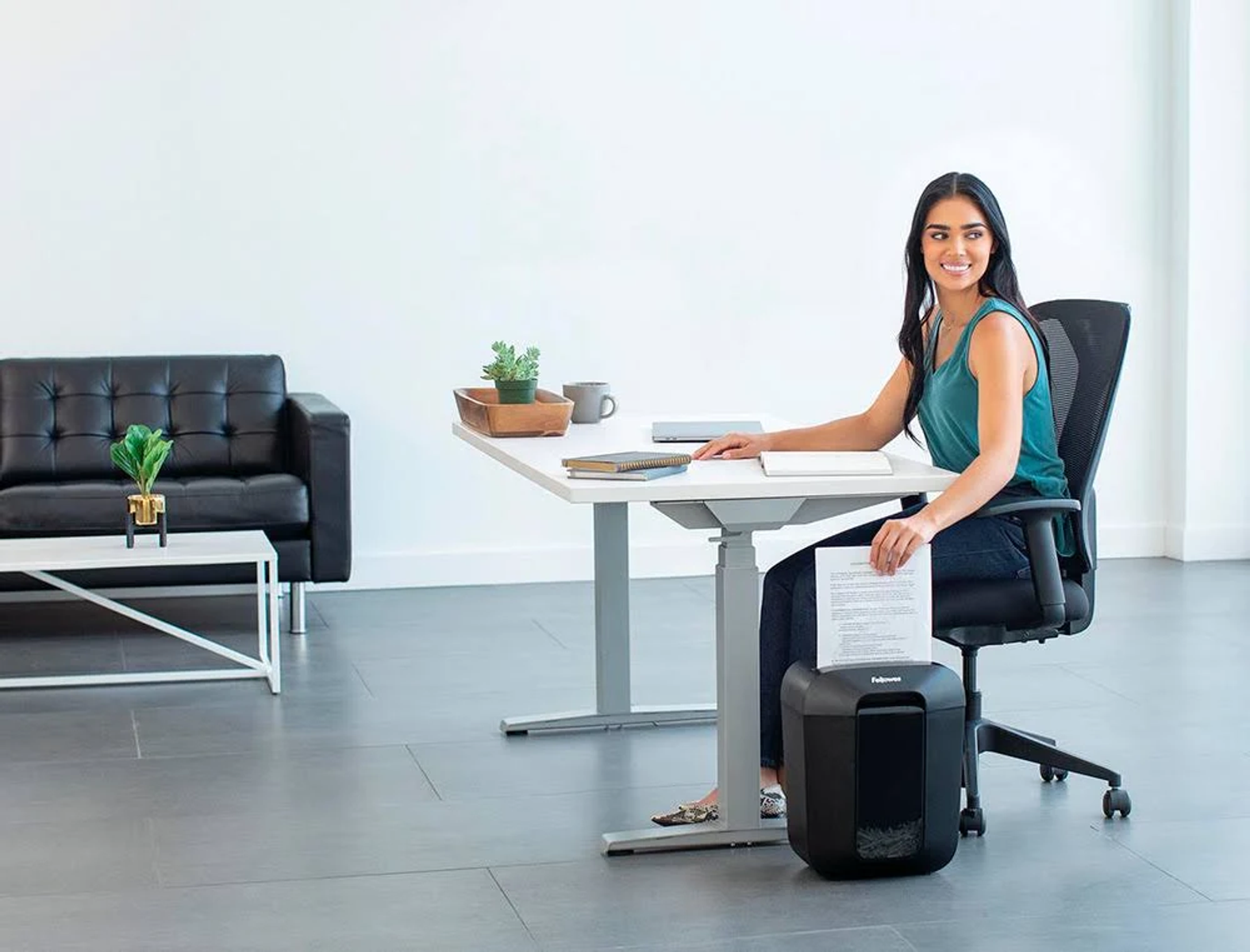 Femme déchiquetant des papiers, assise à un bureau avec une déchiqueteuse noire.