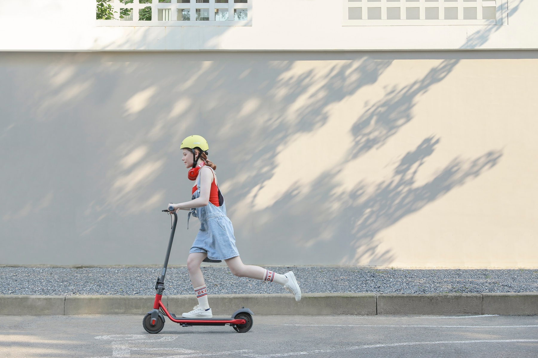 Una ragazza che va in scooter rosso sulla strada, con un casco giallo e una maglietta rossa.