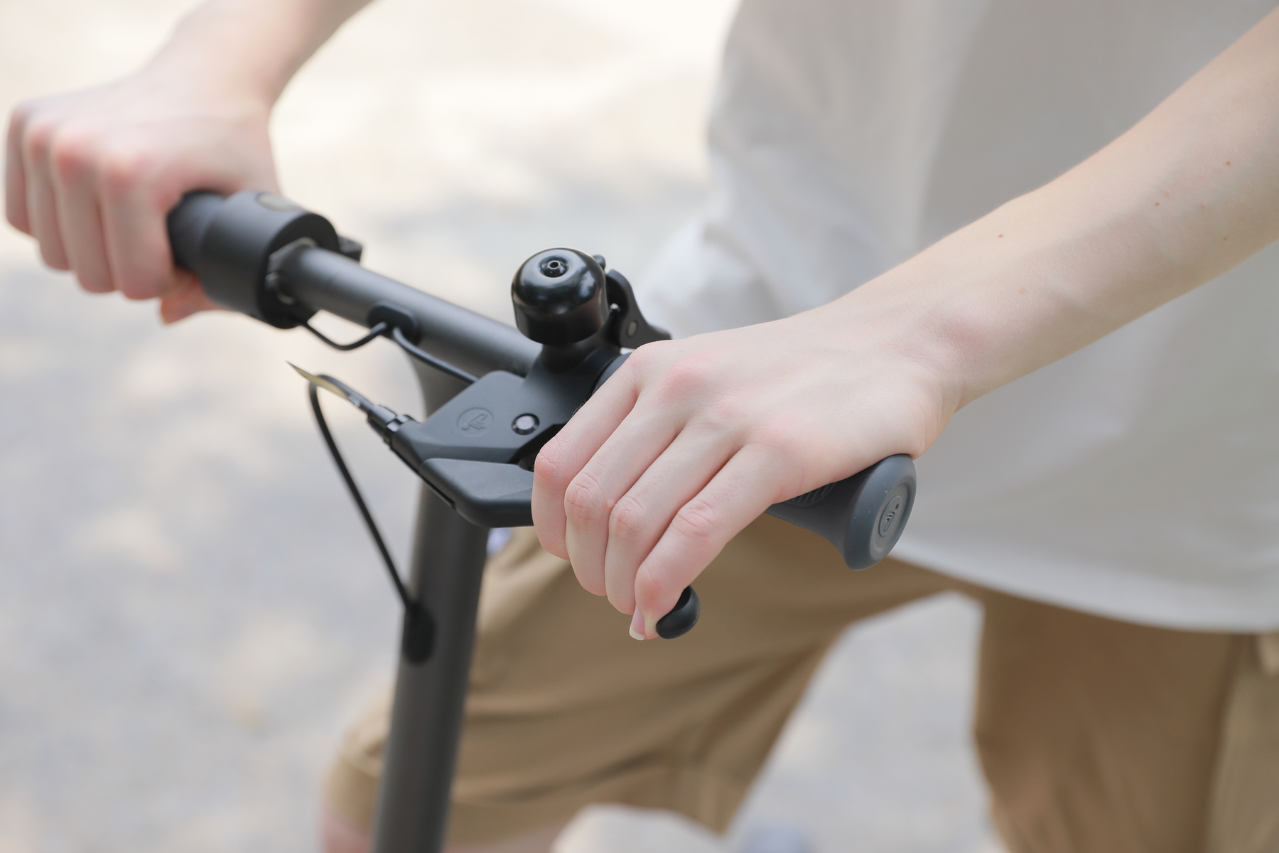 Mani sul manubrio dello scooter. Manubrio nero, campanello e leva freno.