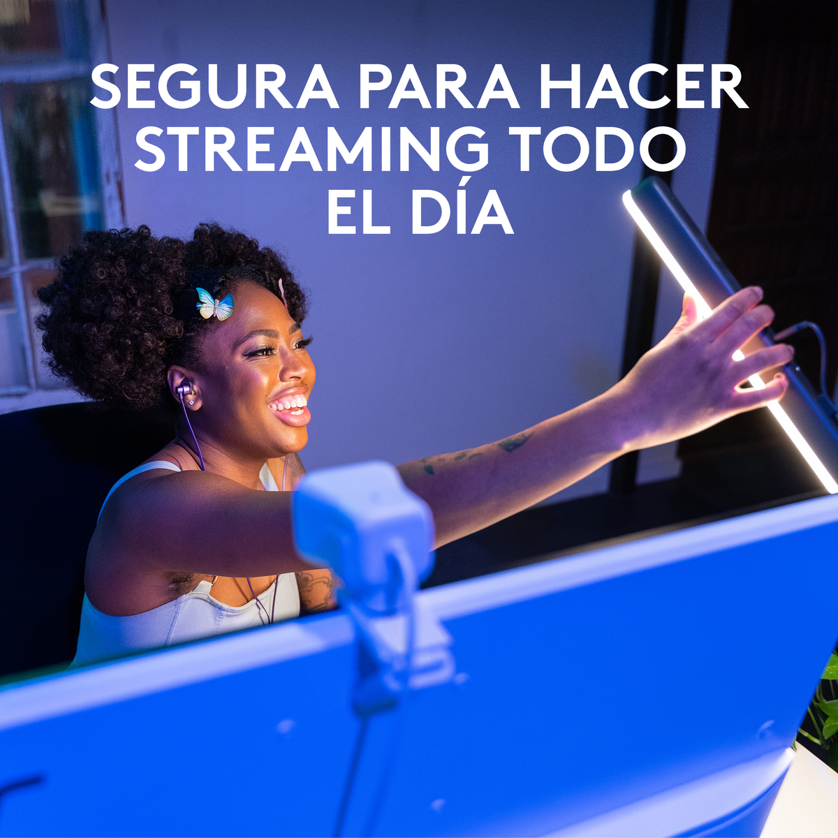 Mujer sosteniendo una luz, sonriendo, cerca de un monitor. Texto dice: 'Seguro para streaming todo el día'.