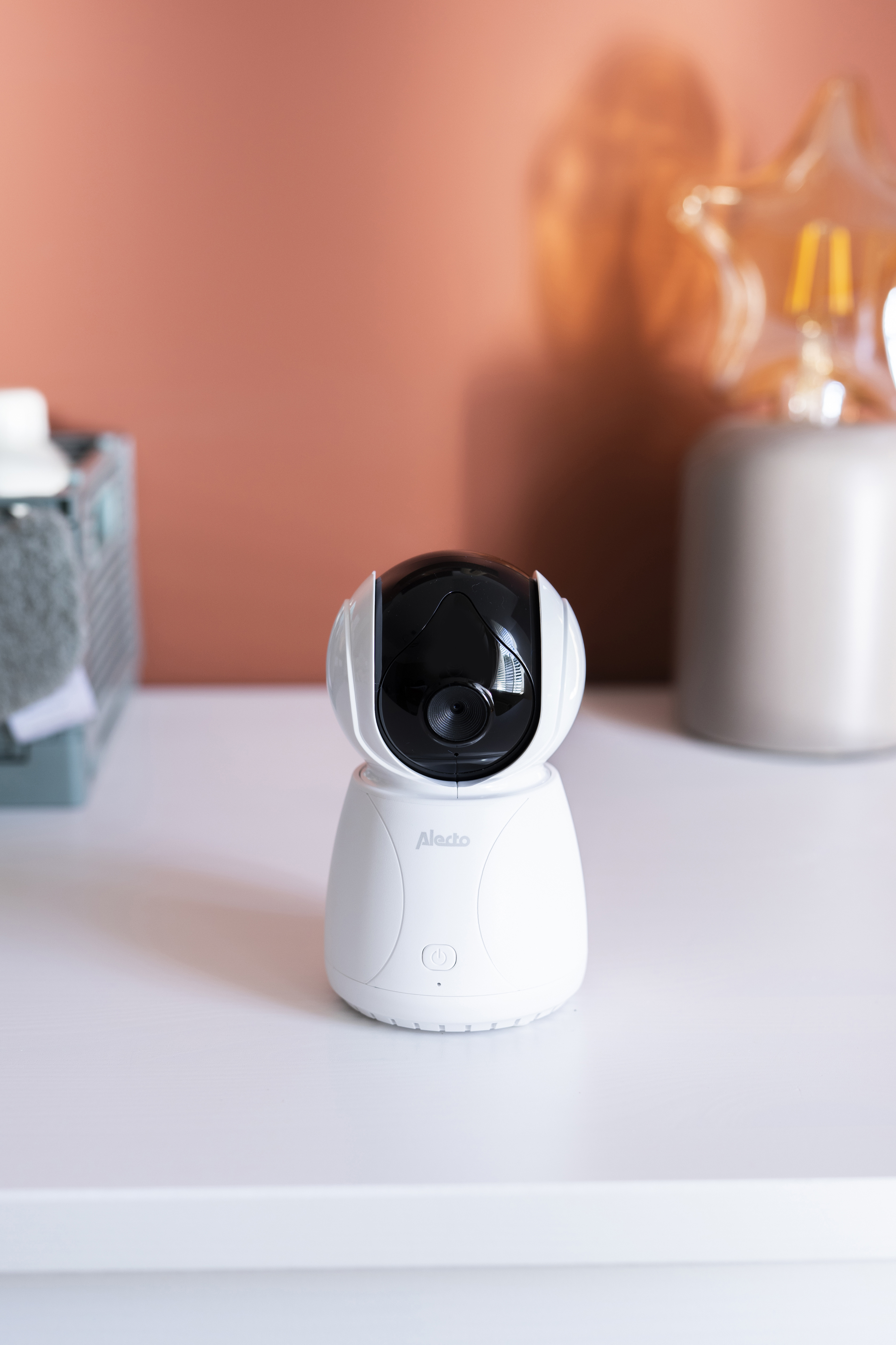 Una cámara de monitor para bebés blanca con parte superior y lente negras, sobre una superficie blanca.