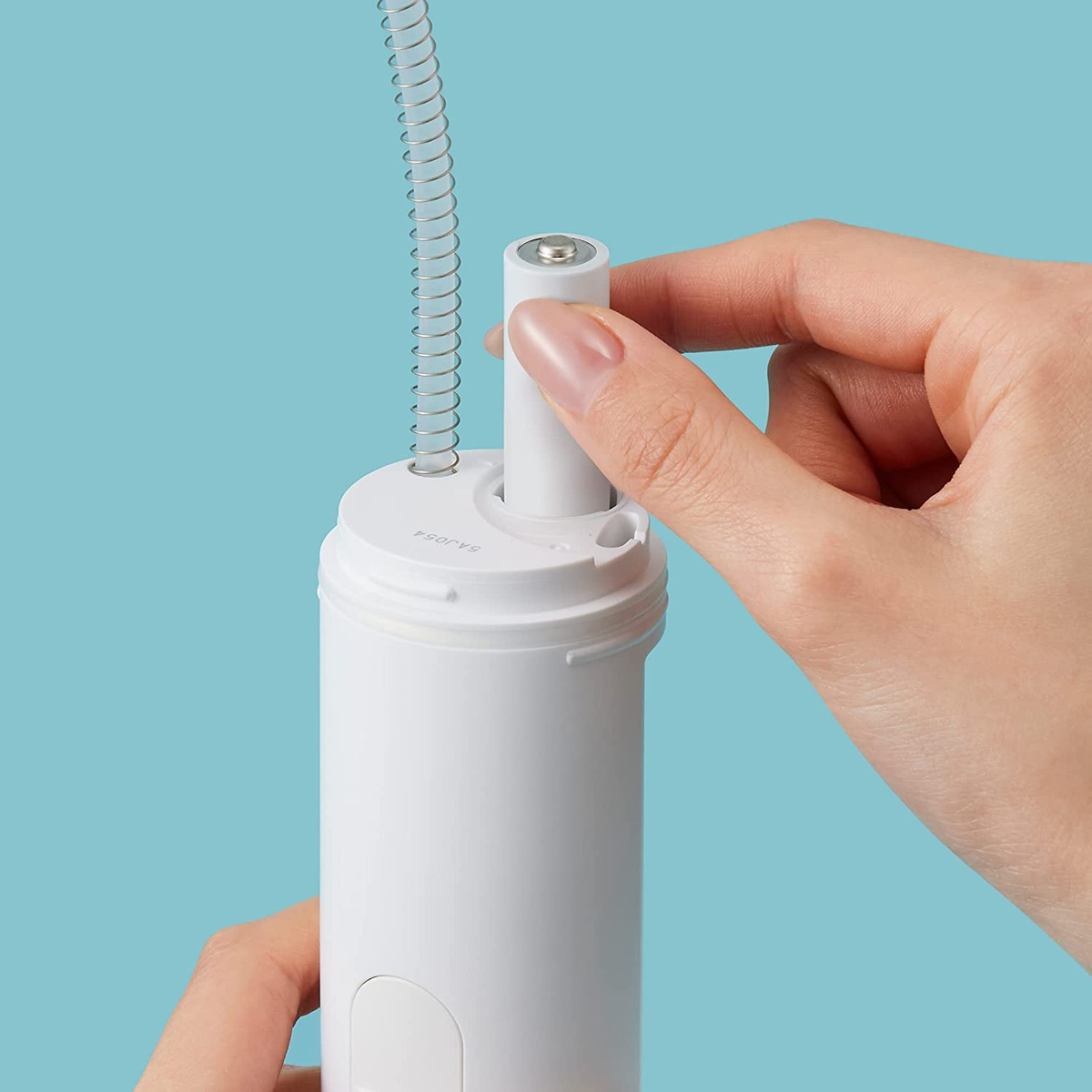 Dłoń wkładająca baterię do białego urządzenia na niebieskim tle.