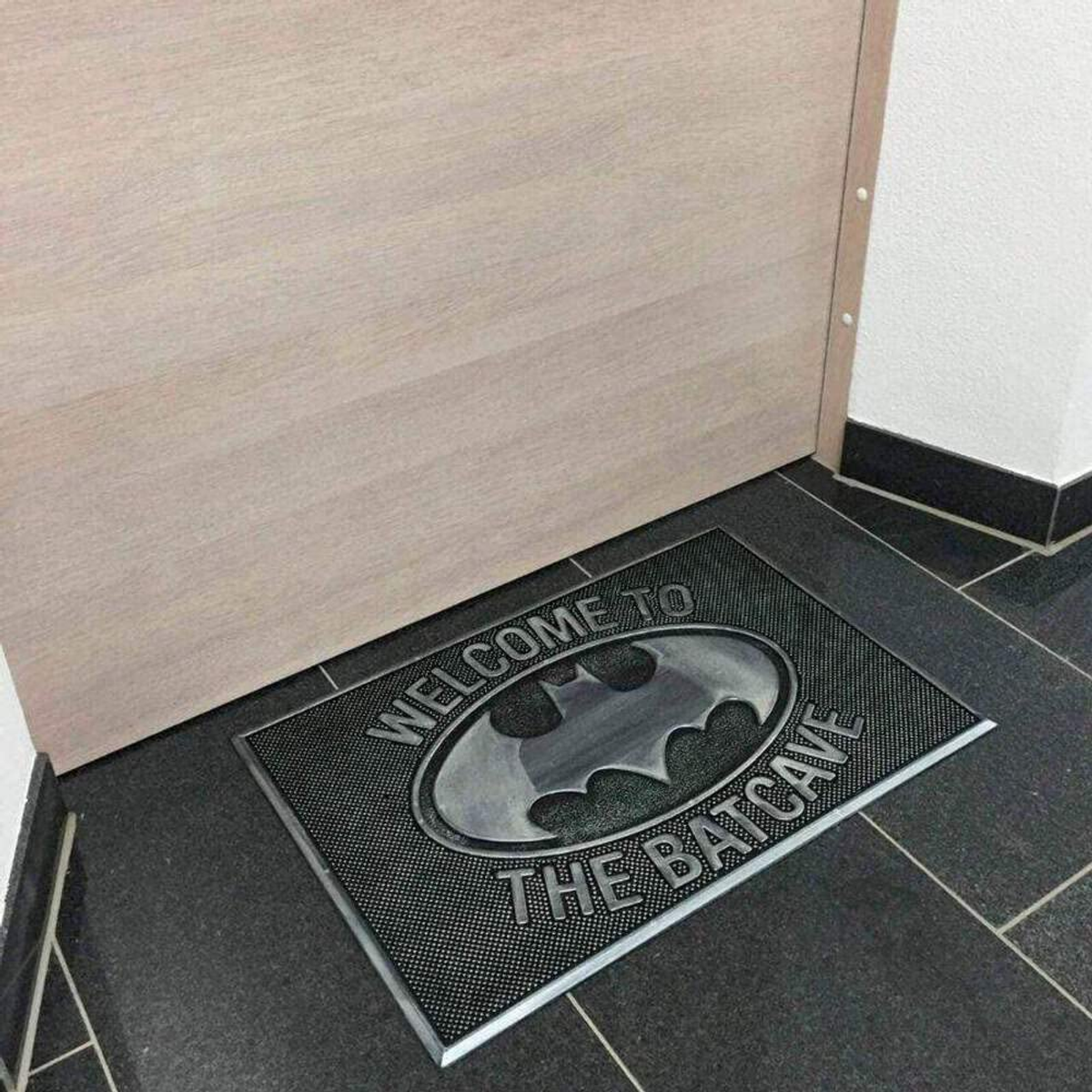 Willkommen-Matte an einer Tür. Die Matte hat das Batman-Logo und die Worte 'Welcome to the Batcave'.