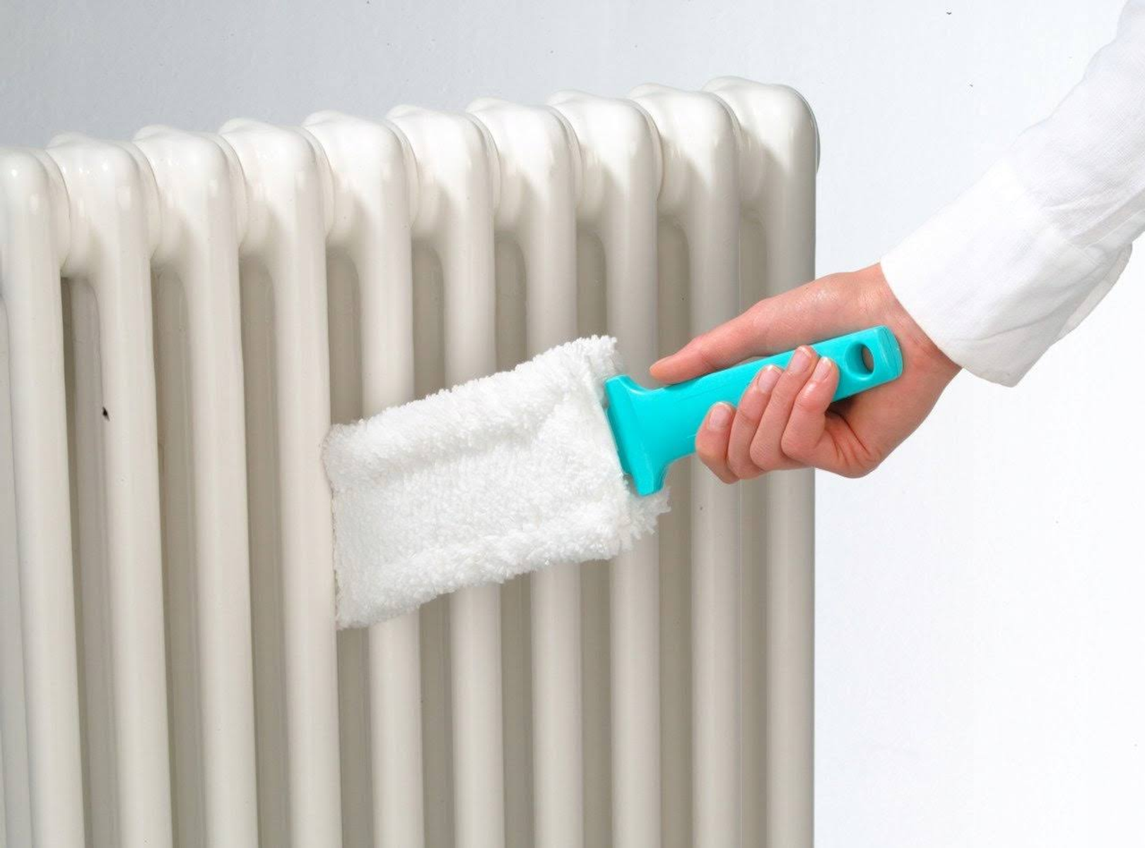 Persona limpiando un radiador blanco con un cepillo con mango azul. Mano enfocada.