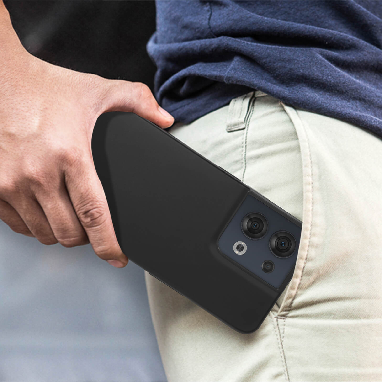 Une main tenant un téléphone noir dans la poche. Le téléphone a plusieurs caméras. Pantalon beige.