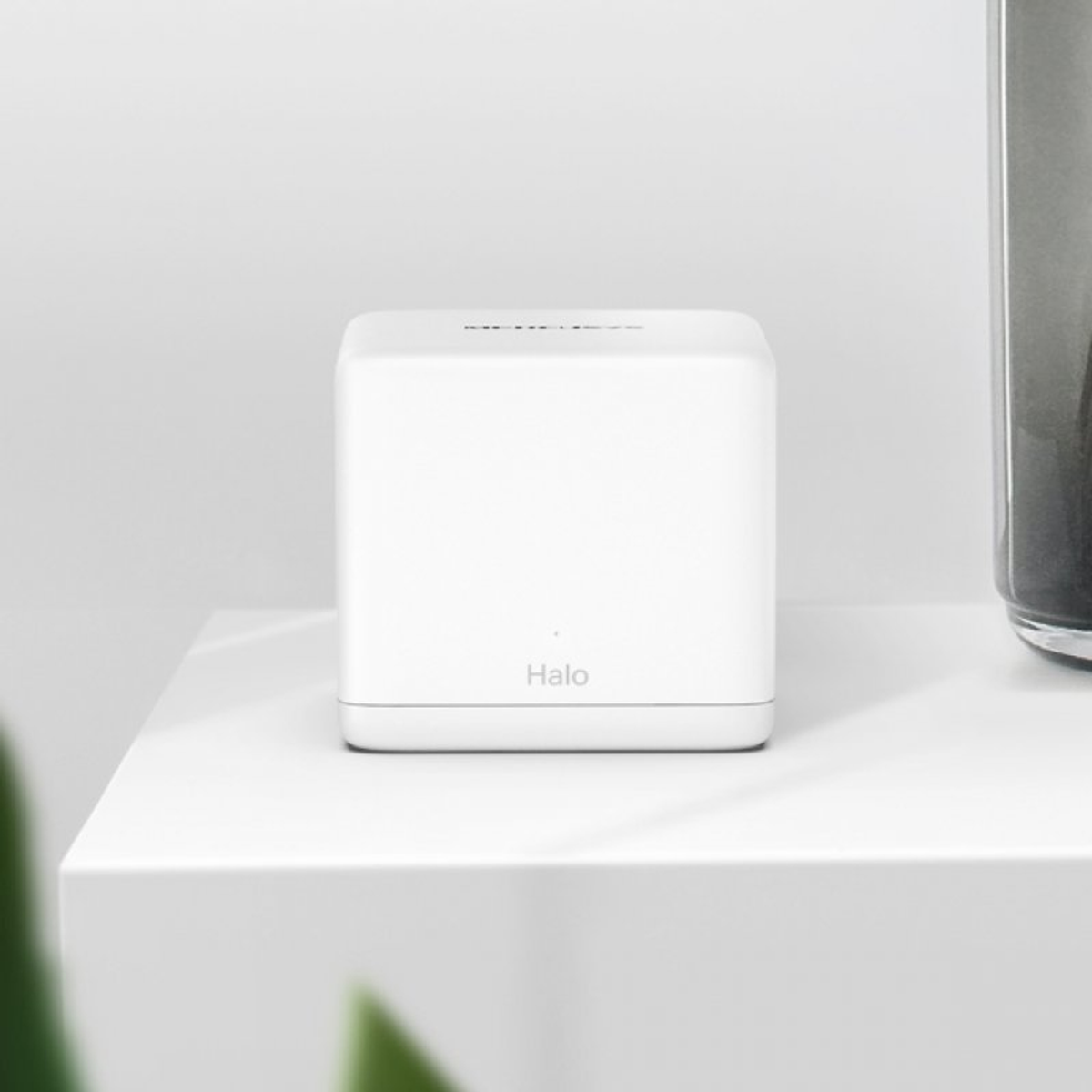 Un cubo Halo blanco sobre una superficie blanca. Un jarrón oscuro en el fondo.