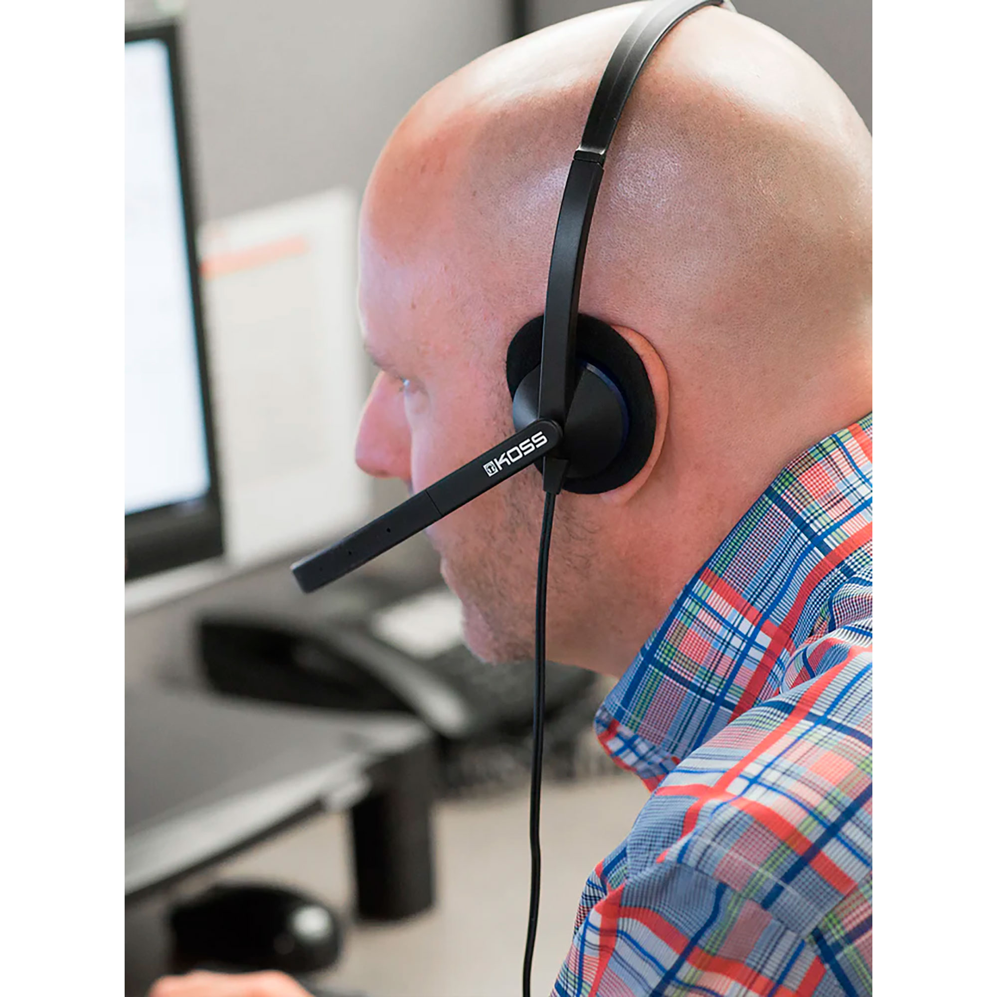 Łysy mężczyzna w czarnym zestawie słuchawkowym z mikrofonem. Zestaw słuchawkowy ma logo 'KOSS'.