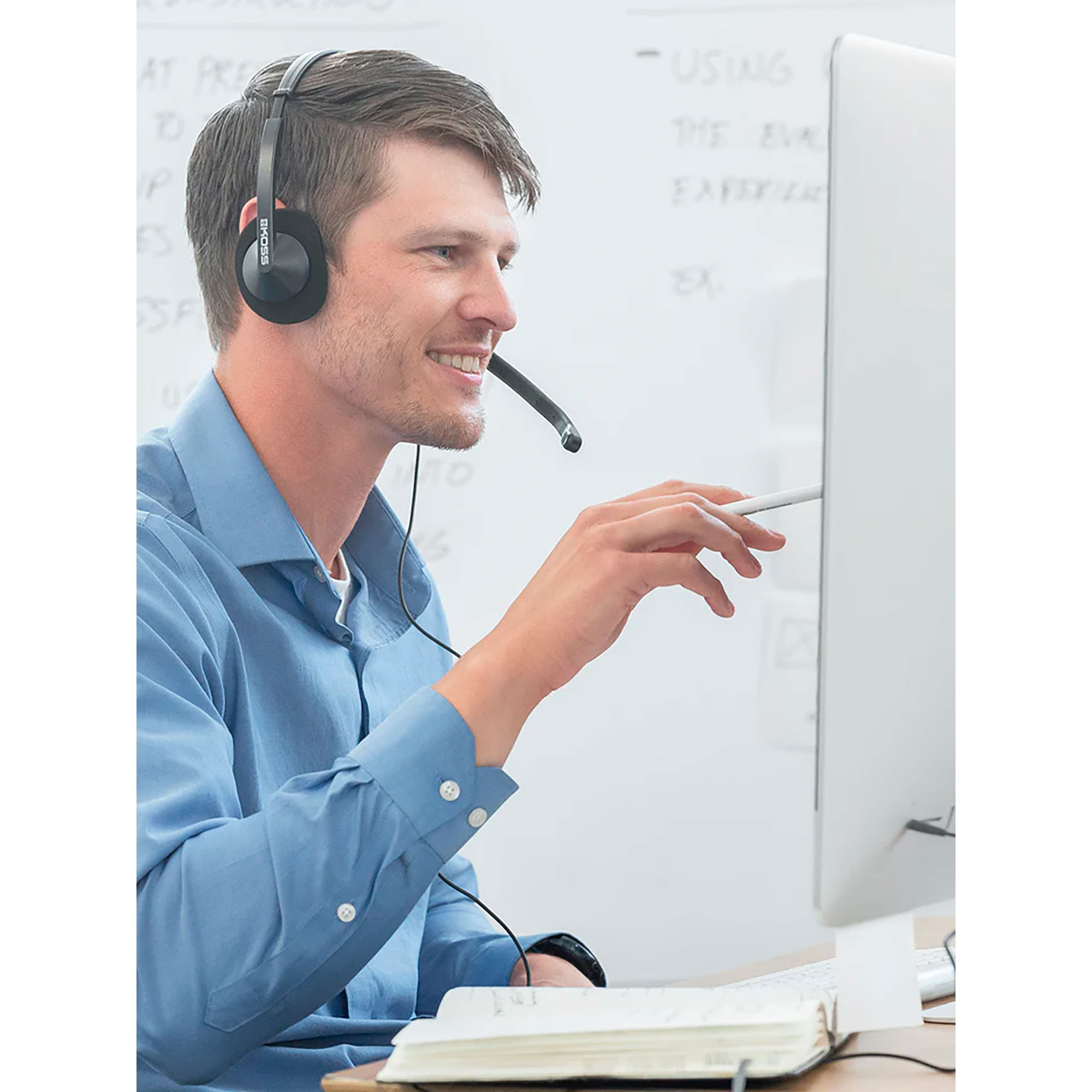 Mężczyzna z zestawem słuchawkowym patrzy na ekran komputera, na biurku notatnik.