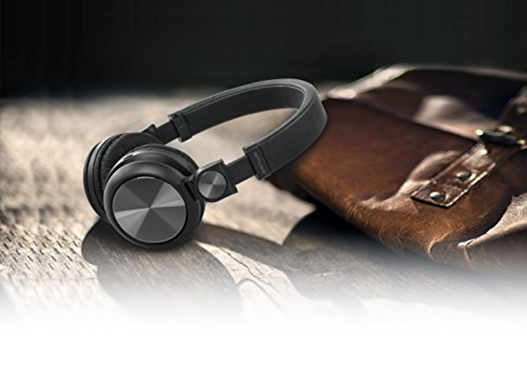 Czarne słuchawki leżące na brązowej skórzanej torbie na białej powierzchni.