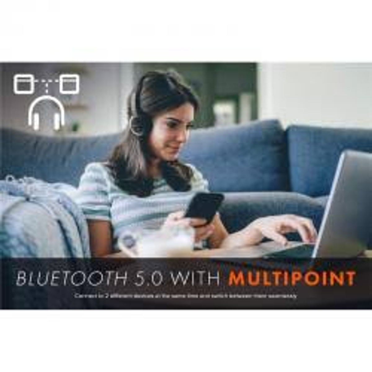 Kobieta siedzi na kanapie korzystając z laptopa, mając na sobie słuchawki i trzymając telefon.