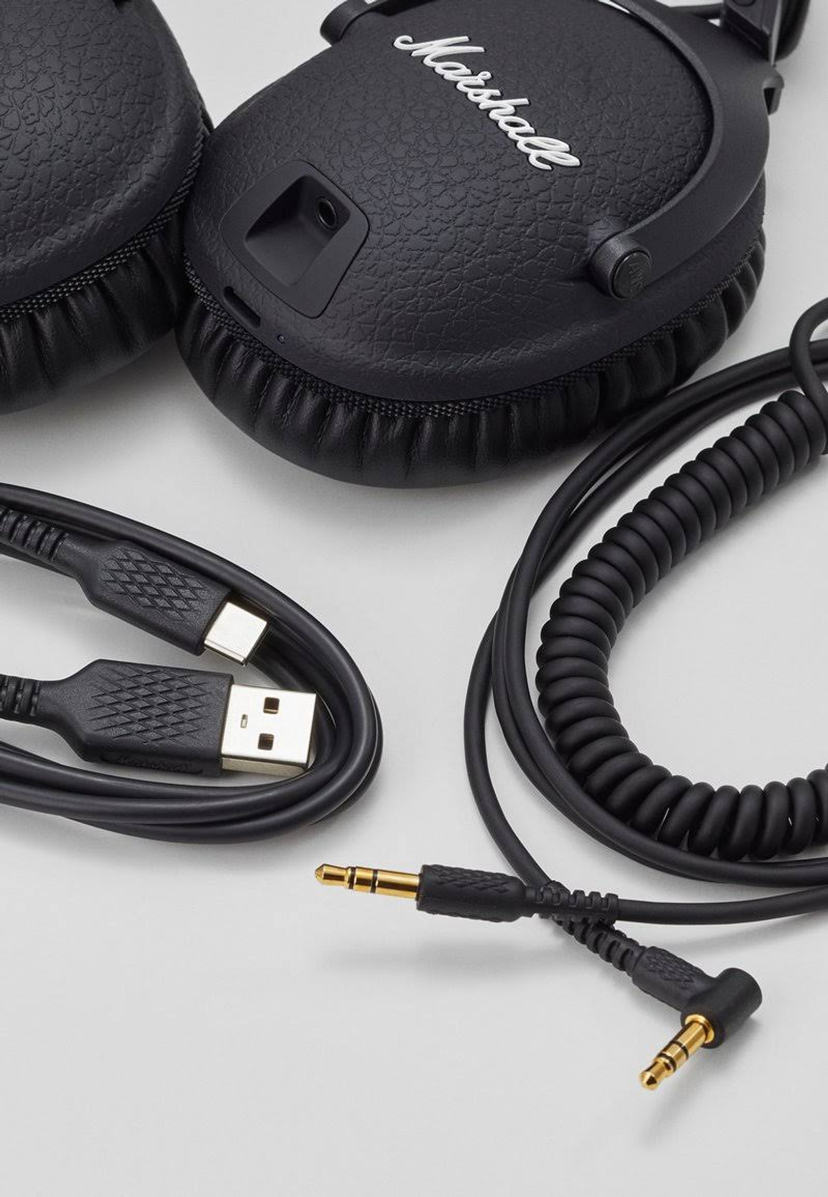 Auriculares Marshall negros, cables USB y de audio junto a ellos.