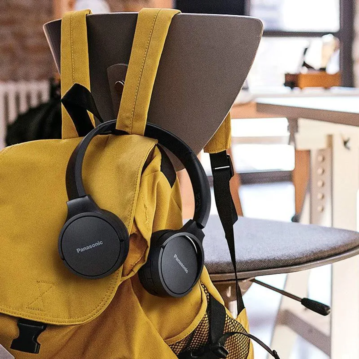 Schwarze Kopfhörer auf einem gelben Rucksack, der an einem Stuhl hängt. Inneneinrichtung.