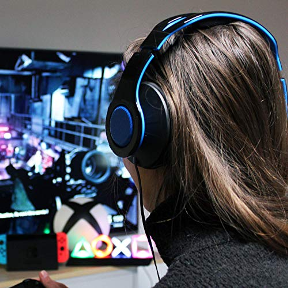 Persona con auriculares de juego, mirando la pantalla. Logos de Xbox, Playstation y Nintendo en el fondo.