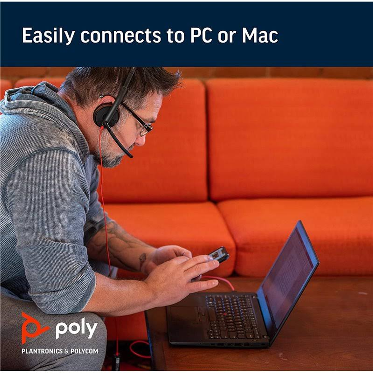 Mann mit Headset nutzt Laptop und Smartphone auf orangefarbener Couch.