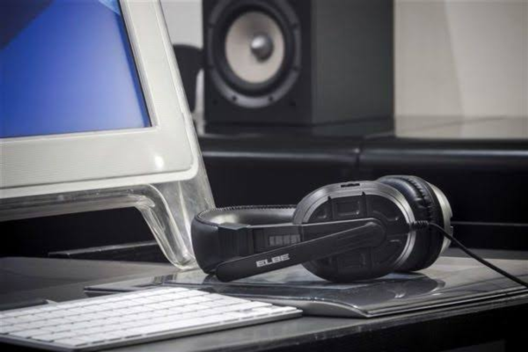 Auriculares negros con micrófono, en un escritorio. Teclado y ordenador visibles.