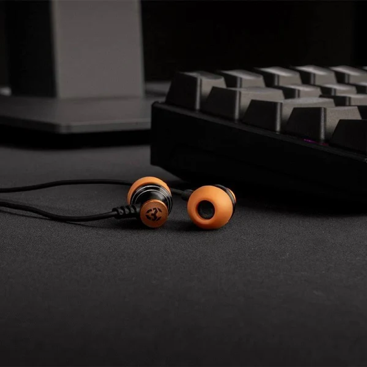 Ohrhörer auf schwarzem Untergrund. Die Ohrhörer sind orange und schwarz. Eine Tastatur ist im Hintergrund.