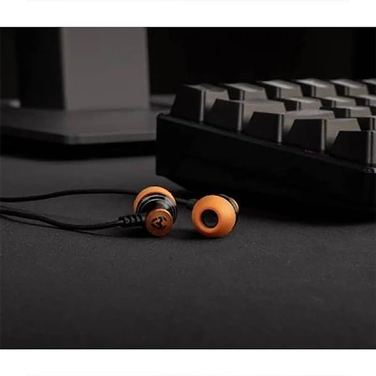 Ohrhörer mit orangefarbenen Ohrstöpseln und schwarzem Kabel, vor einer Tastatur. Dunkler Hintergrund.