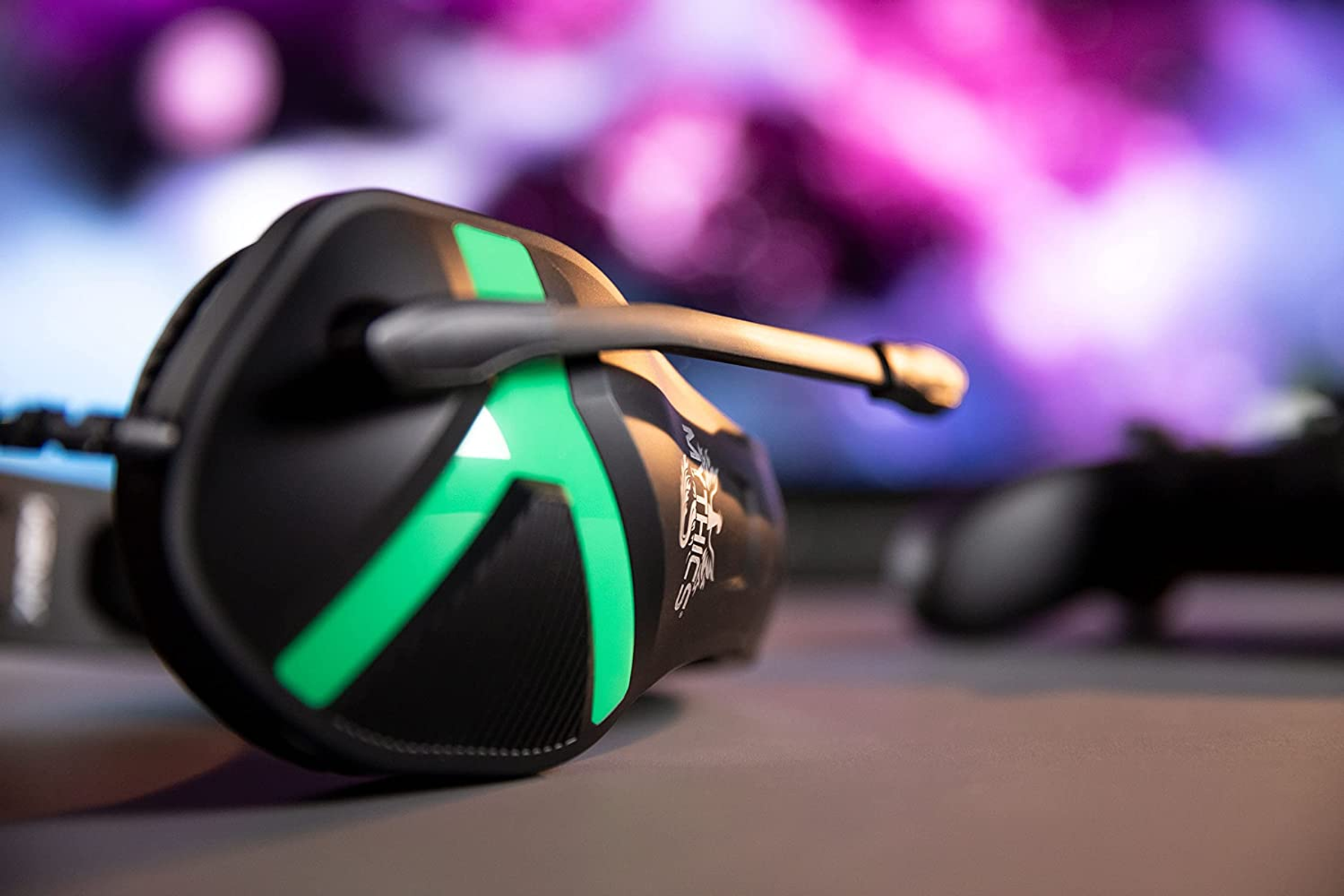 Zestaw słuchawkowy dla graczy w konfiguracji gamingowej. Zestaw jest czarny i zielony, na biurku, rozmyte tło.