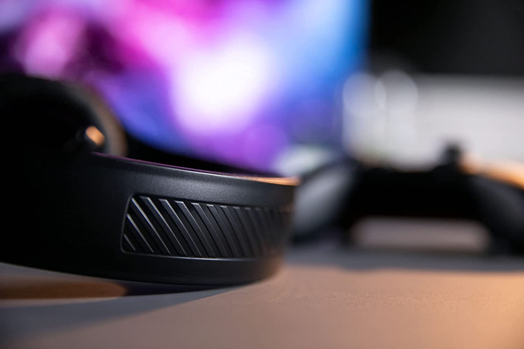 Zbliżenie czarnych słuchawek. Niewyraźne tło z ekranem i gamepadem.