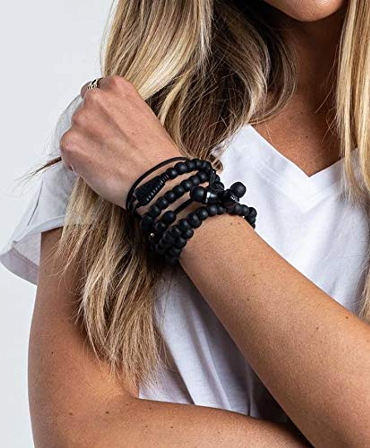 Arm einer Frau mit schwarzen Perlenarmbändern, weißem Hemd und Silberring.
