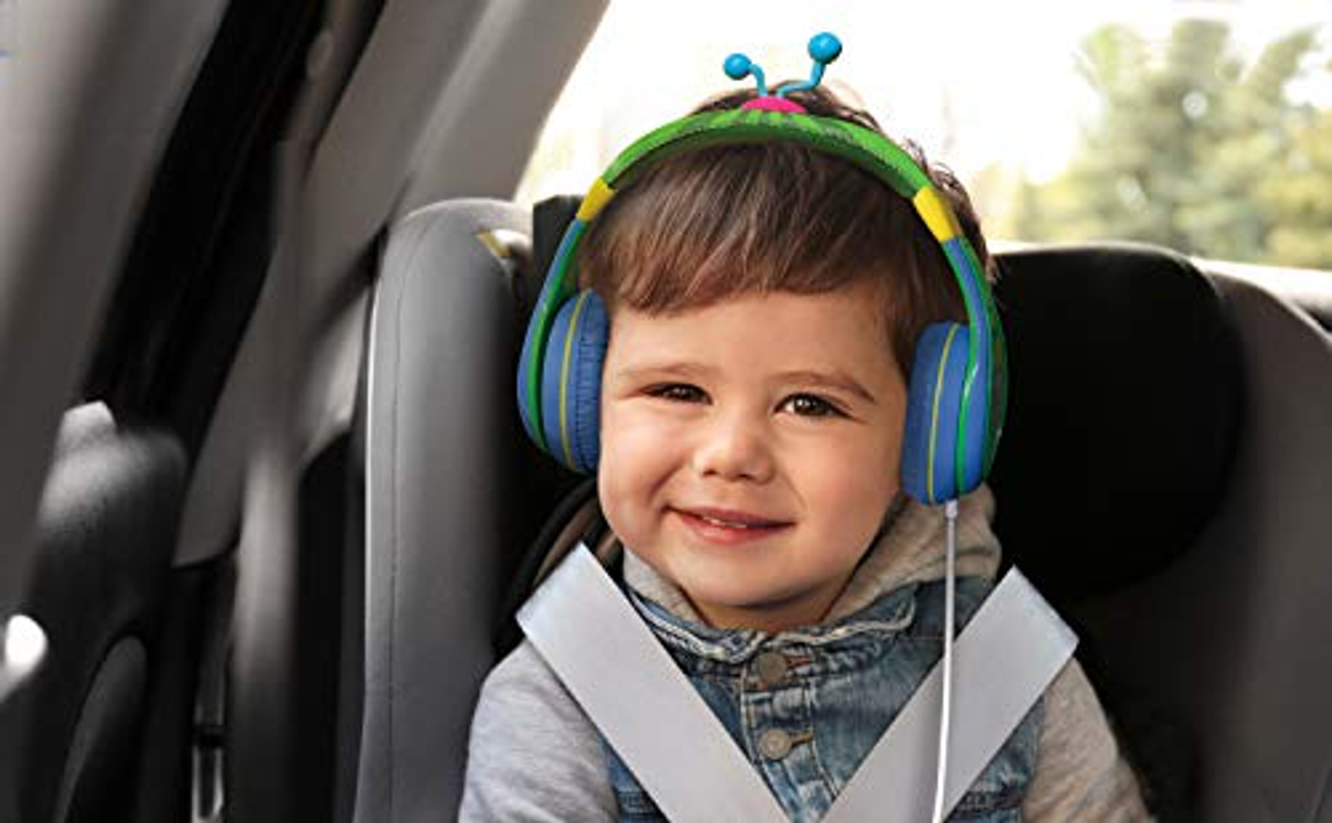 Bambino sorridente in un seggiolino per auto con cuffie a tema insetti blu e verdi.